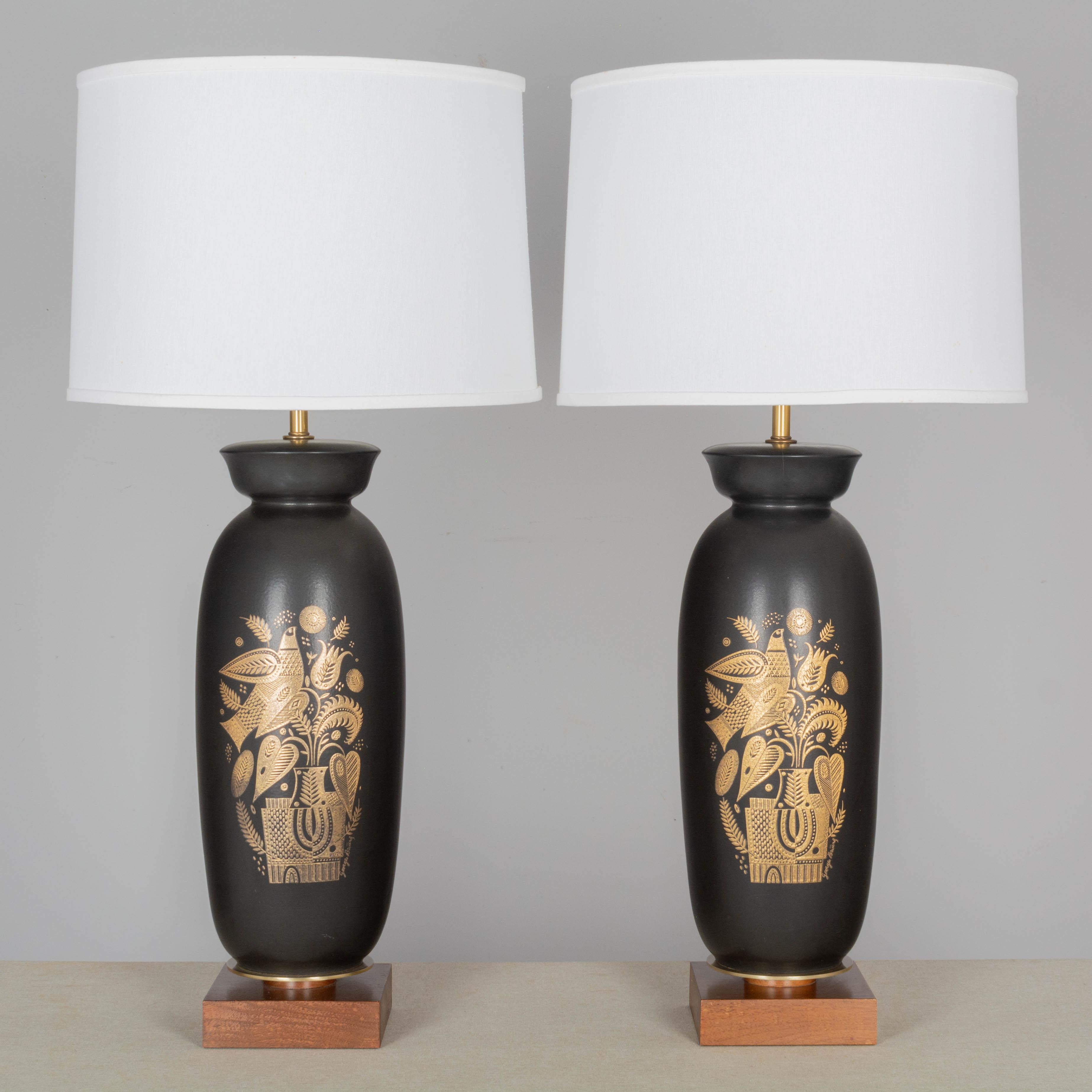 A pair of iconic Midcentury Modern ceramic lamps by Georges Briard. Tall matte black ceramic body with gold decoration of a stylized bird and potted plant. Square wood base with brass disc. New socket, cord and brass finials. Please see photos for