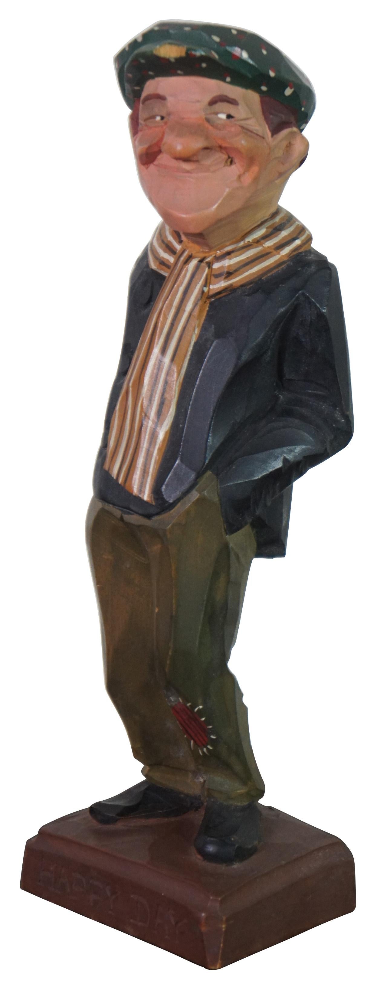 Mid century carved wood folk art figure by Gerald Pat Hannah titled “Happy Day,” featuring a man with patched trousers, striped scarf and spotted cap, standing with his hands in his pockets, once smoking a cigar. “One of the original three Hannah