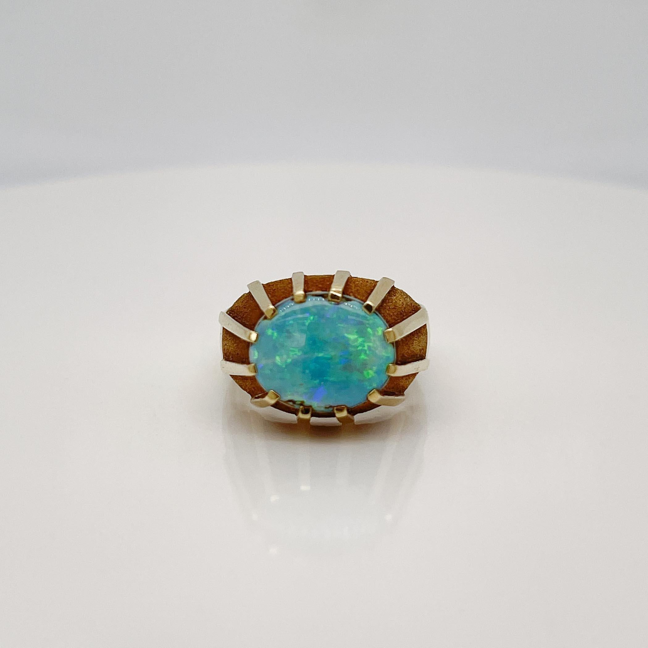 A fine German Mid-Century gold and opal ring.

In 14k yellow gold. 

Prong set with a smooth oval opal doublet. 

Each smooth prong extends into the design of the ring and alternates with gold textured surfaces. The opal doublet has a beautiful