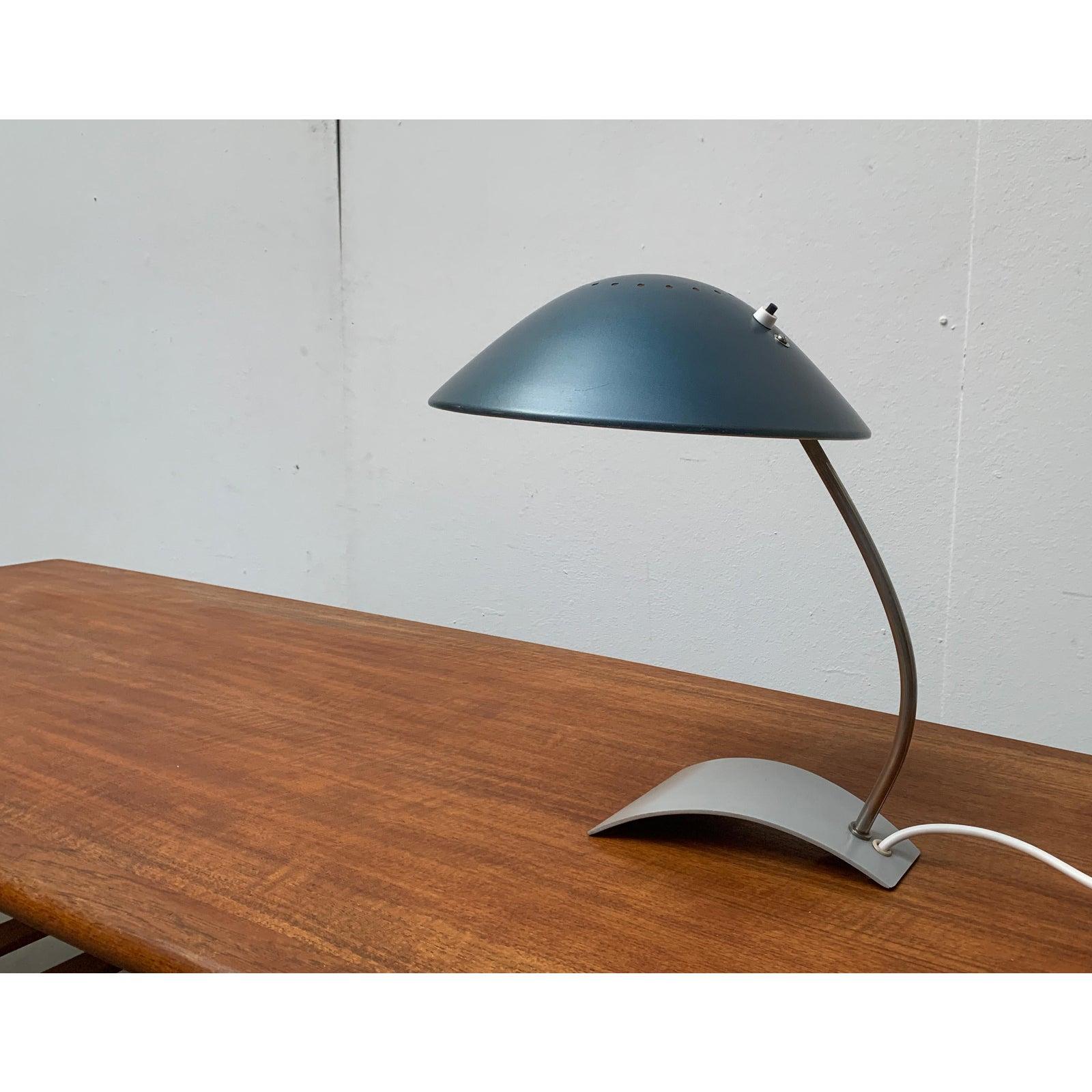 Elegante lampe de table de Kaiser Leuchten.

Le détail particulier de cette lampe est sa base, qui est simplement de la tôle pliée. La perforation radiale sur le dessus de l'abat-jour projette un léger éclat dans la pièce. Cette pièce porte une