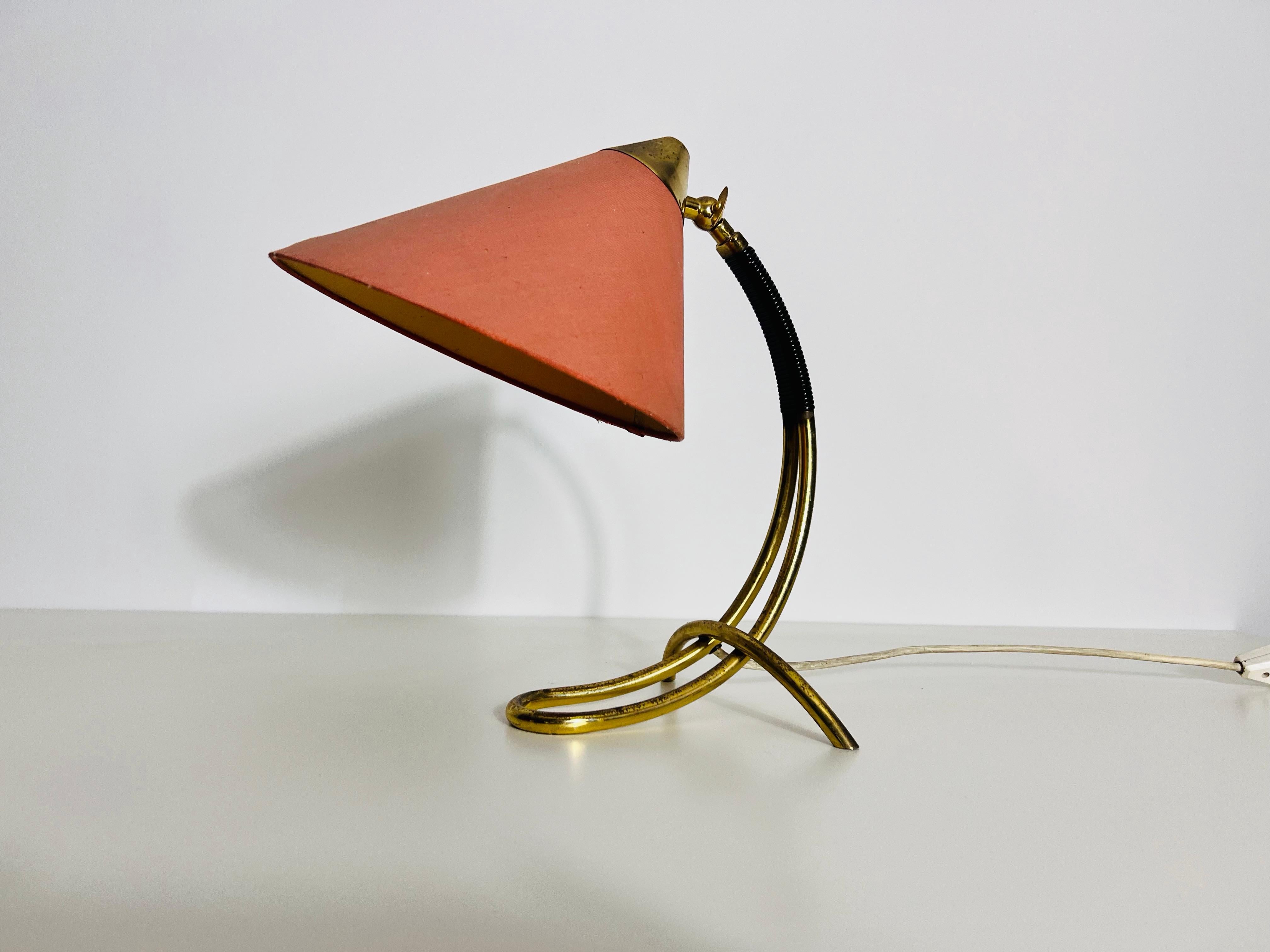 Cette lampe de table raffinée en laiton allemand des années 1960 incarne l'élégance du design moderne du milieu du siècle dernier. Son corps épuré en laiton, façonné dans une forme tubulaire, se dresse gracieusement sur trois pieds élancés en