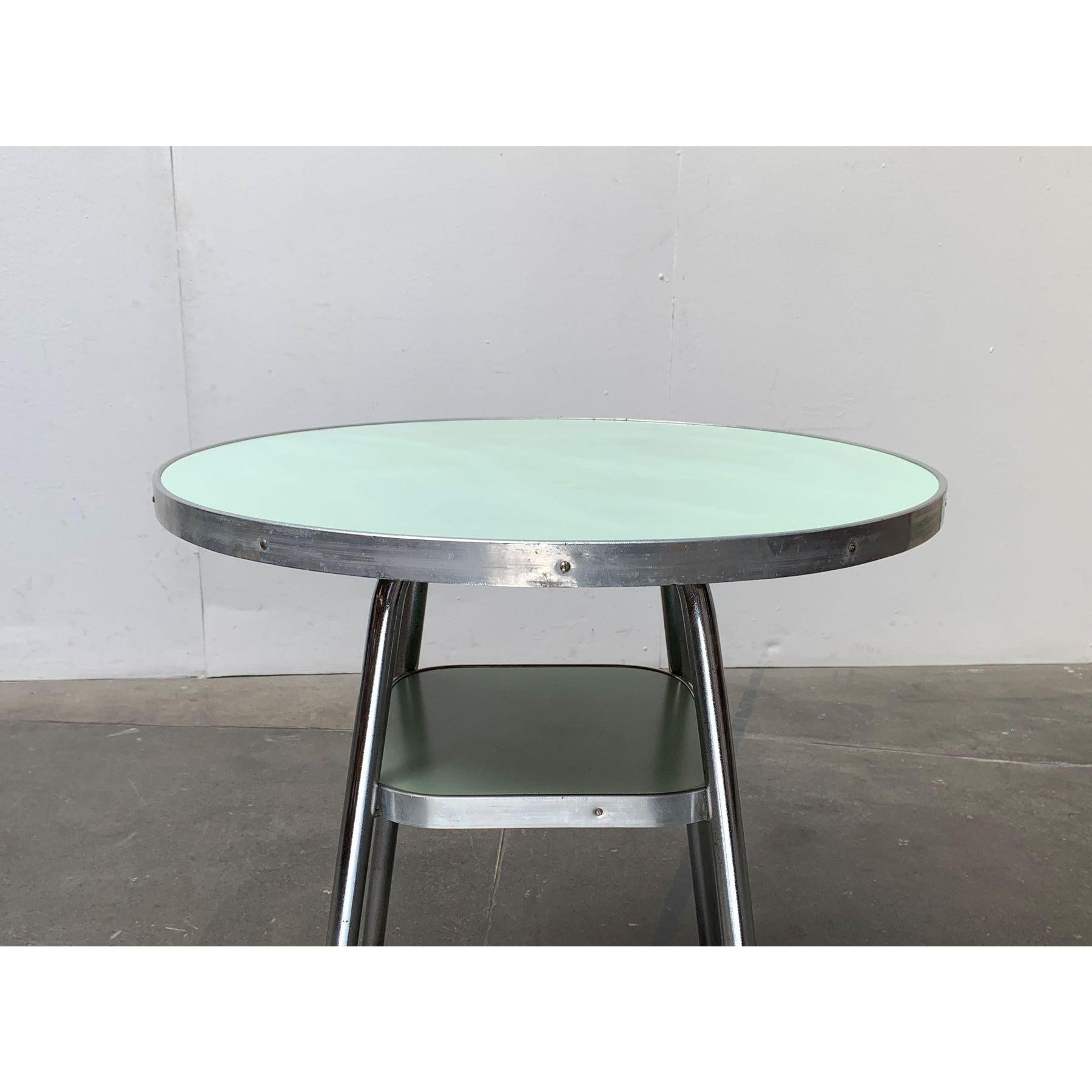 Table Mauser en tube d'acier avec étagère.

Le revêtement coloré de la surface de la table ronde attire particulièrement l'attention. La couleur est répétée dans l'étagère ci-dessous. Les pieds du cadre sont en tube d'acier chromé et élégamment