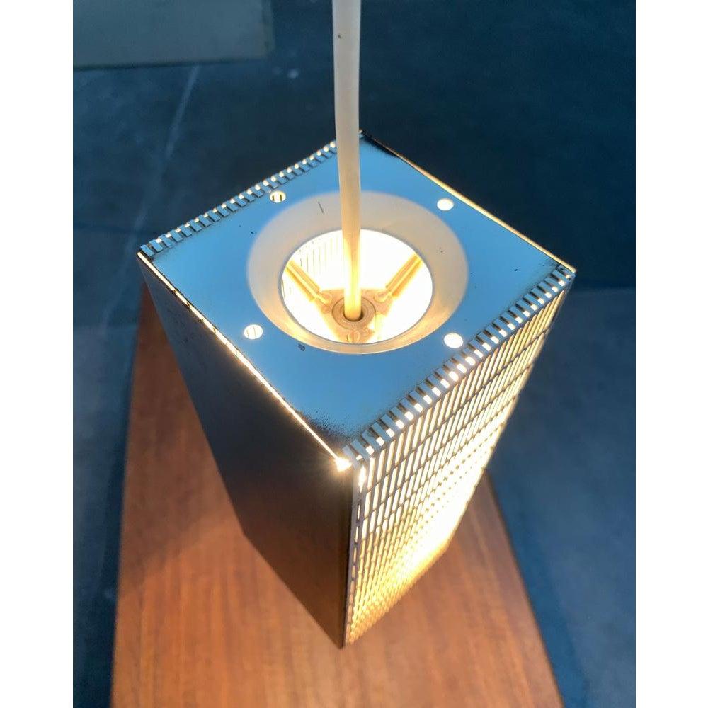 Lampada a sospensione di metà secolo con elementi in lamiera forata.

Un design minimalista. Il corpo luminoso ha la forma di un semplice cuboide. Due lati del cuboide sono chiusi e dipinti di nero. Gli altri due lati sono progettati in lamiera