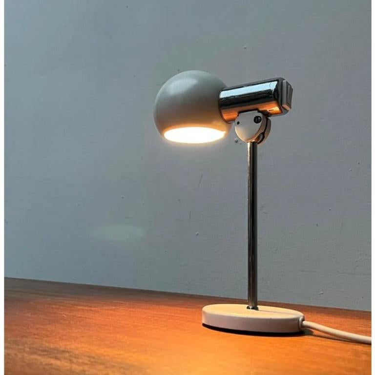Rares lampes de table de Kaiser Leuchten.

La tête d'éclairage se compose d'un cylindre chromé relié à un arbre chromé par une rotule. La tige élancée se termine par un pied simple en forme de plaque blanche. Un interrupteur se trouve à l'arrière de