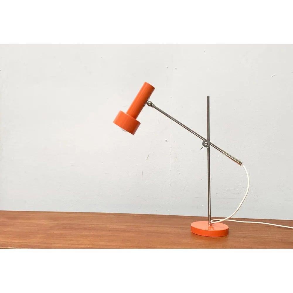 Minimalist mid-century table lamp from Beisl in a special color.

The minimalist spotlight shape of the lamp head is striking. Two simple cylinders of different sizes. The orange of the head is repeated in the heavy plate base of the lamp. The