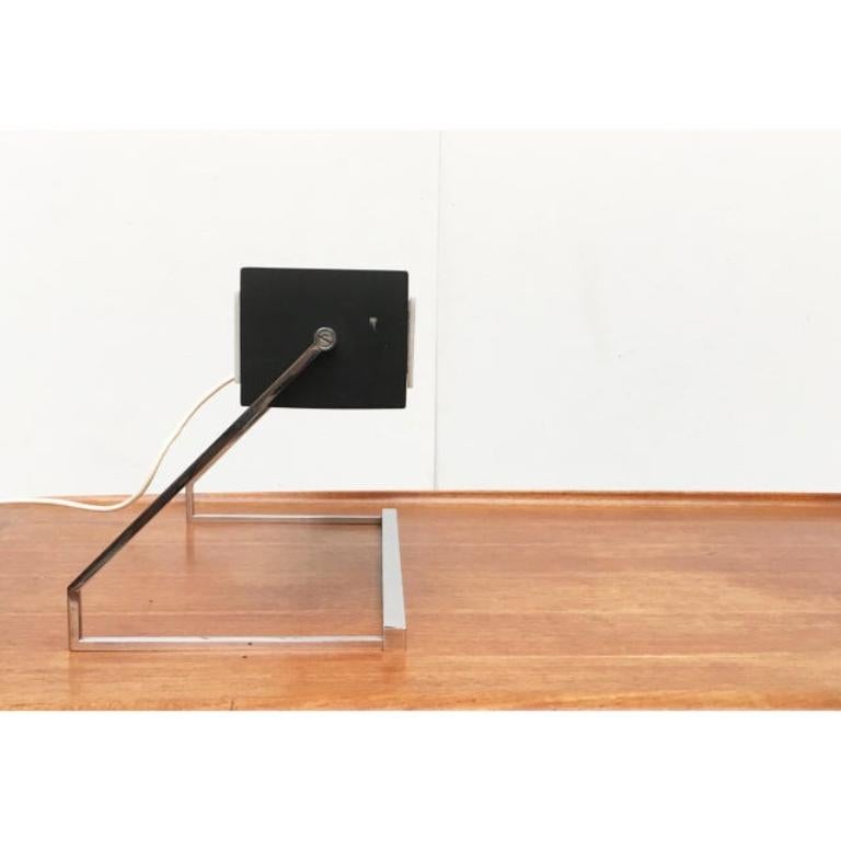 Minimalist Mid Century desk lamp from Cosack.

A very linear and delicate design. The cuboid body made of painted metal sheet is open at the bottom. At the front and back translucent acrylic discs are used as diffusers. The finely finished frame is