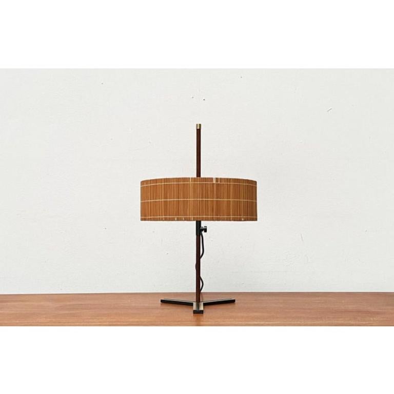 Very rare mid-century table lamp from the German manufacturer Kaiser Leuchten.

The design impresses with its special materiality. The simple drum shade is covered with a raffia-like material. The shade can be moved up and down the shaft to change