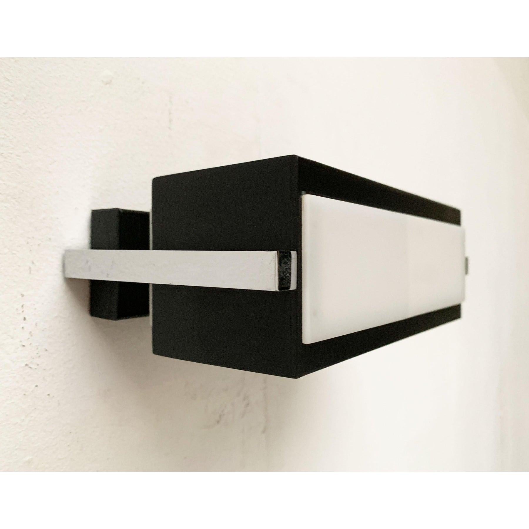Lampada da parete minimalista del Mid Century di cosack. Un design molto semplice e filigranato. Il corpo cuboide in lamiera verniciata è aperto sul fondo. Sul lato anteriore e posteriore vengono utilizzati come diffusori dei dischi acrilici