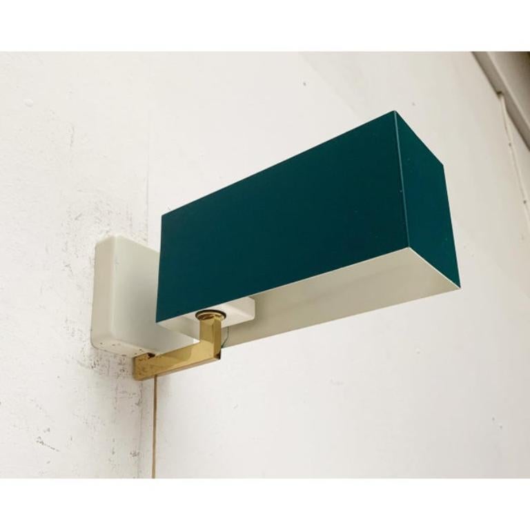 Aplique sencillo Mid Century de Kaiser lights.

Un diseño minimalista. En el extremo de un brazo acodado se asienta una sencilla pantalla rectangular en tono verde oscuro. La pantalla se puede girar y ajustar la luz. La luz tiene un botón para