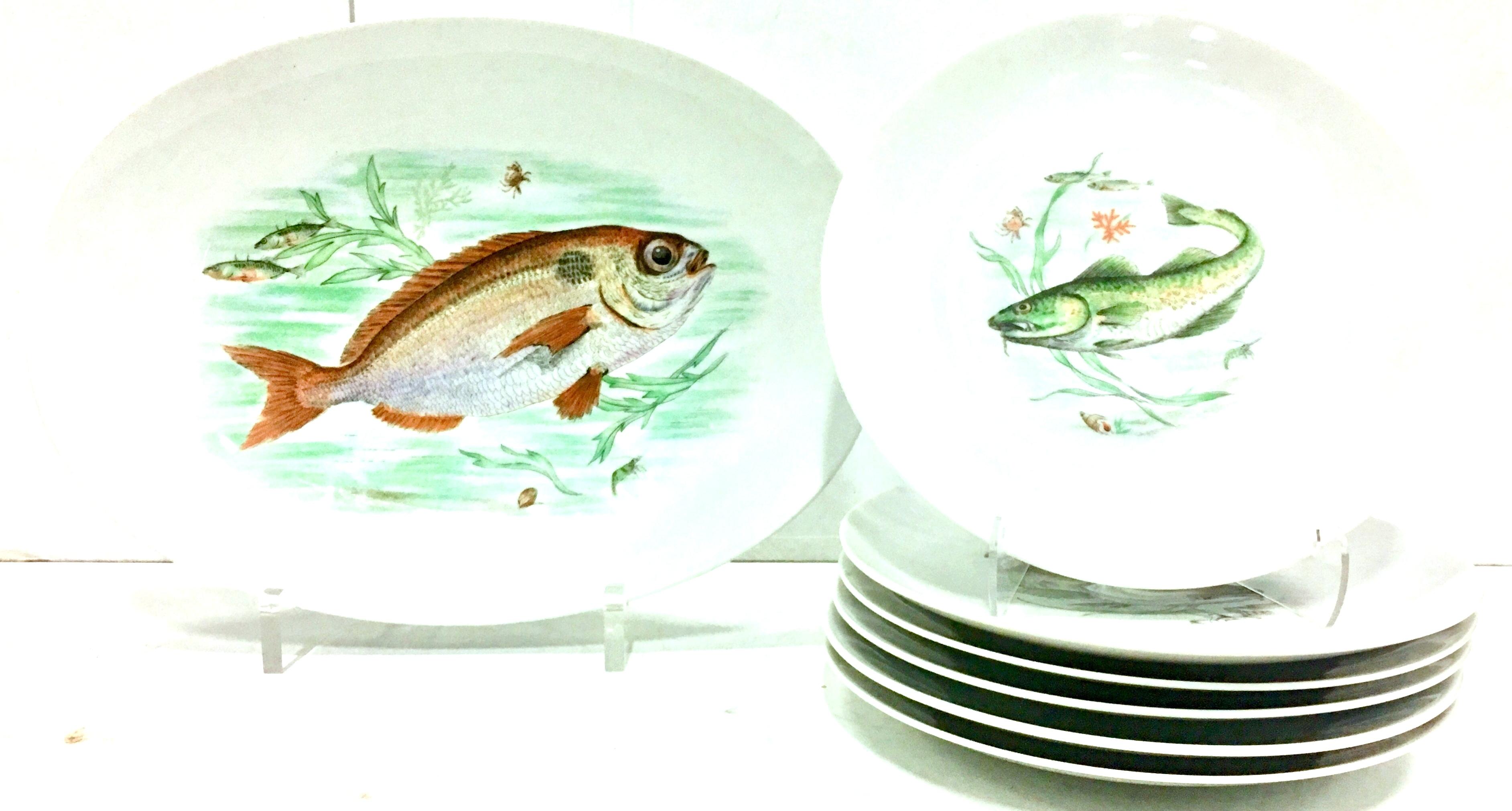 1930s German hand-painted porcelain fish service of seven pieces by, JKW. Set includes six dinner plates, each one a different fish motif and one large oval serving platter. Features a modern clean lined bright white ground with a vibrant earth tone