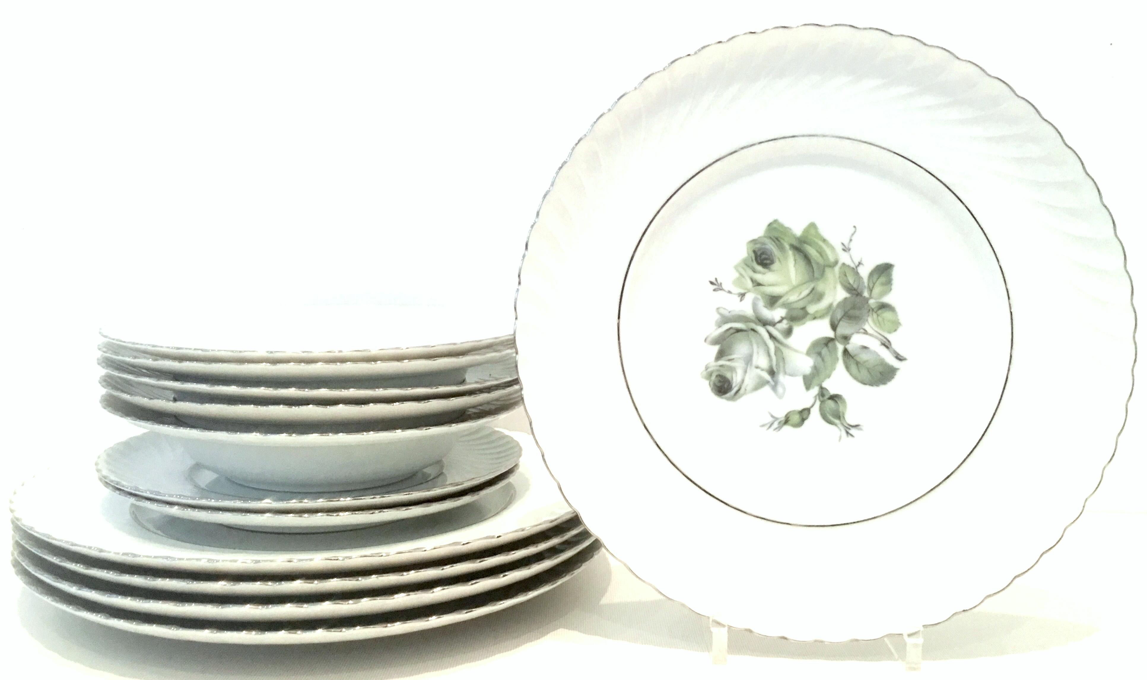 Mid-20th century German porcelain and platinum dinnerware set of twelve pieces by, Royal Tettau.. This German porcelain pattern by Royal Tettau features a bright white ground, swirled edge with a blue and green central rose motif and silver platinum