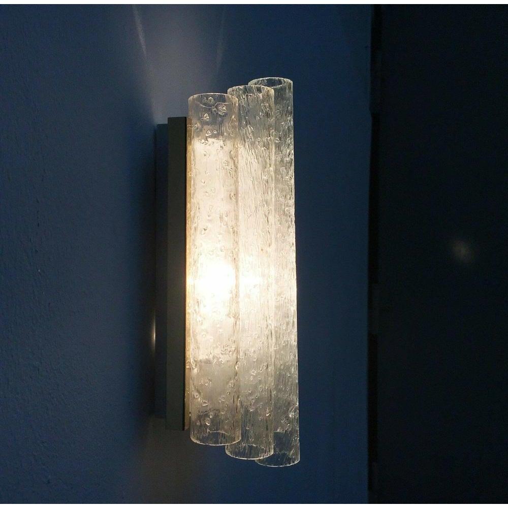 Imponente aplique de cristal del conocido fabricante Doria Leuchten.

Este Doria Leucht lleva colgados en la parte delantera 5 vasos de diferentes longitudes. Los elementos de vidrio estructural rompen y potencian la luz de la lámpara en su