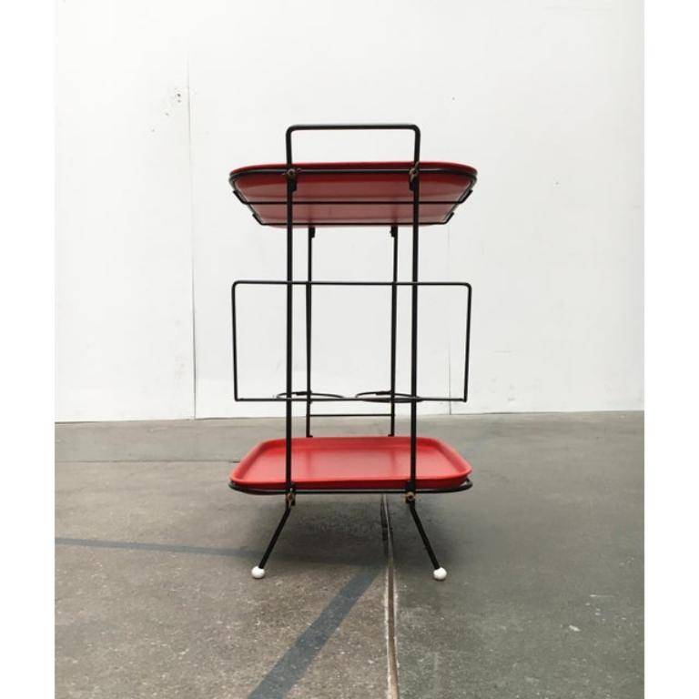 Table filigrane avec plateaux et bar.

Coloration distinctive en rouge et noir. Le cadre finement exécuté se compose de tiges d'acier recouvertes de noir et disposées au-dessus en guise de poignée. Les boules blanches en guise de pieds constituent
