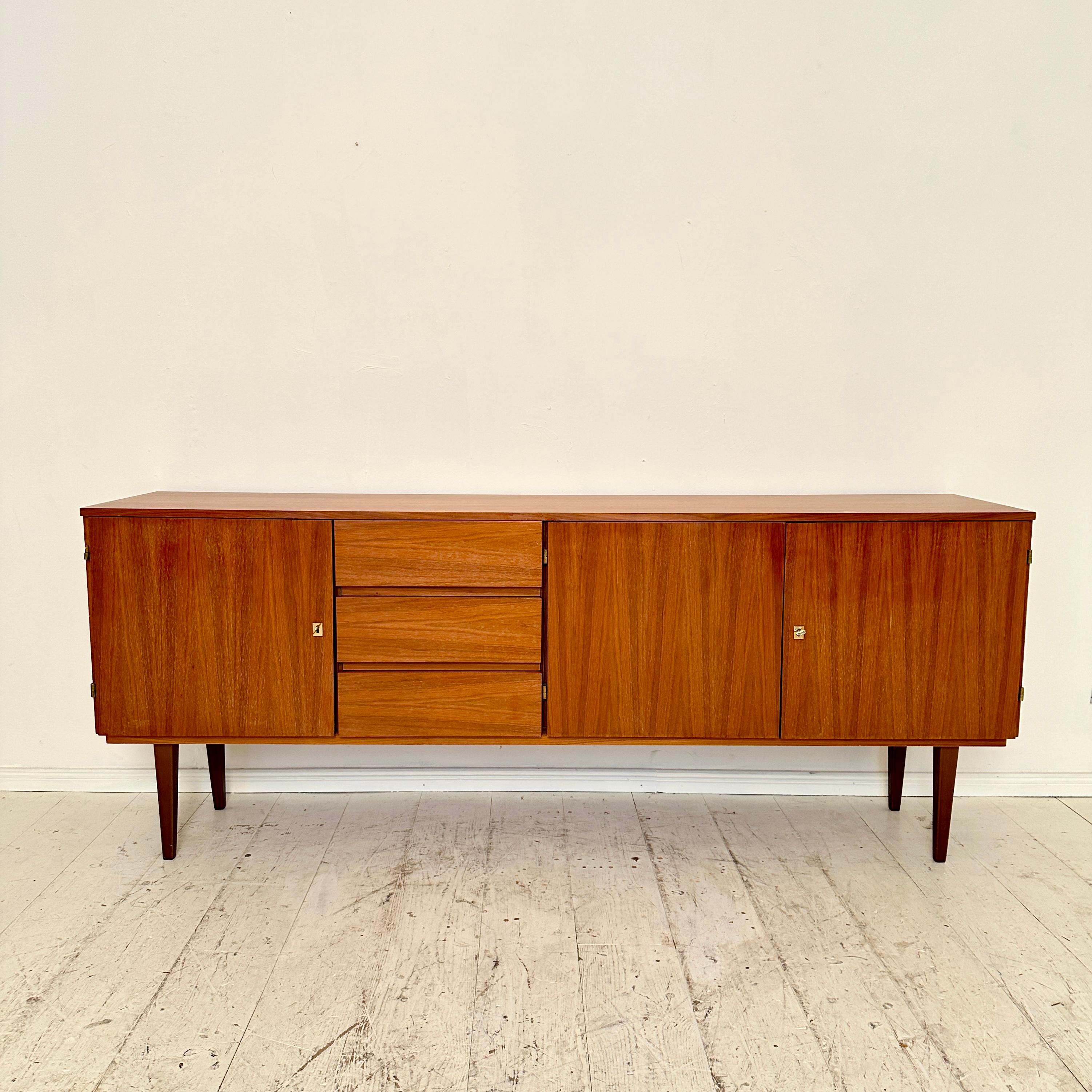 Dating back to the 1960s, this Mid-Century German Sideboard in rich brown walnut is a testament to the era's impeccable design sensibilities. With three drawers and three doors, it seamlessly marries form and function. The warm walnut woodgrain,