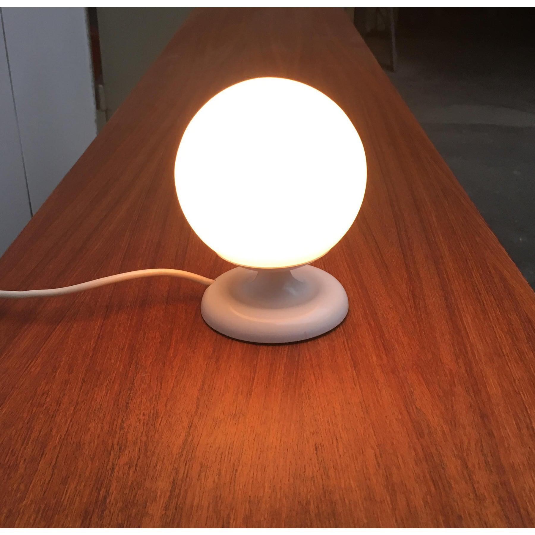 Petite lampe de table à boule du célèbre fabricant Kaiser Leuchten.

Un design simple avec des détails particuliers. La base est ornée d'un petit renfoncement circonférentiel qui constitue un subtil ornement. Le diffuseur en verre opale est placé