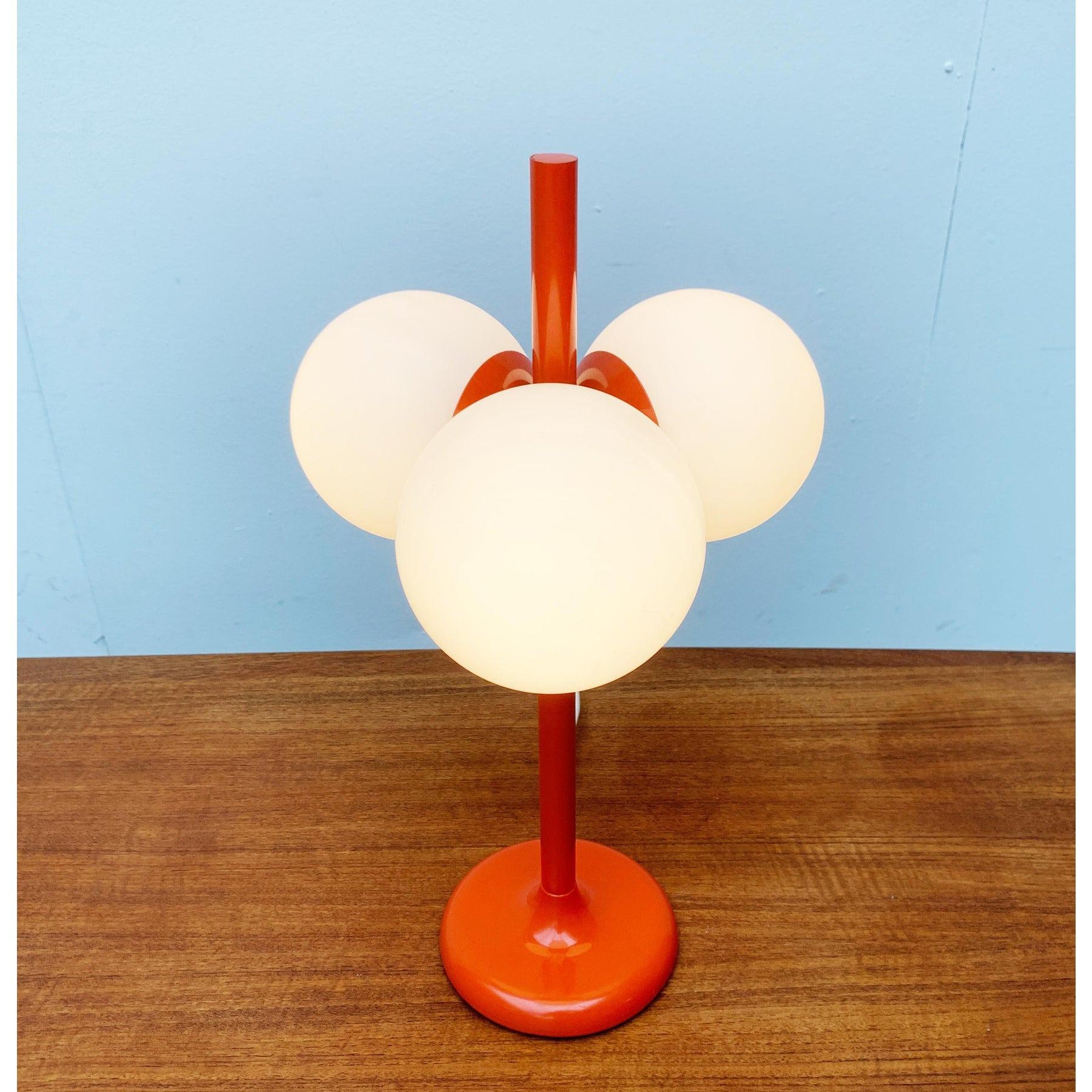 Imposante lampe de table NO AGE de Kaiser Leuchten dans une couleur spéciale.

Le corps central de la lampe est orange. La tige élancée se fond à la base dans un pied en forme de trompette. Les boules de diffusion en verre blanc superposé sont