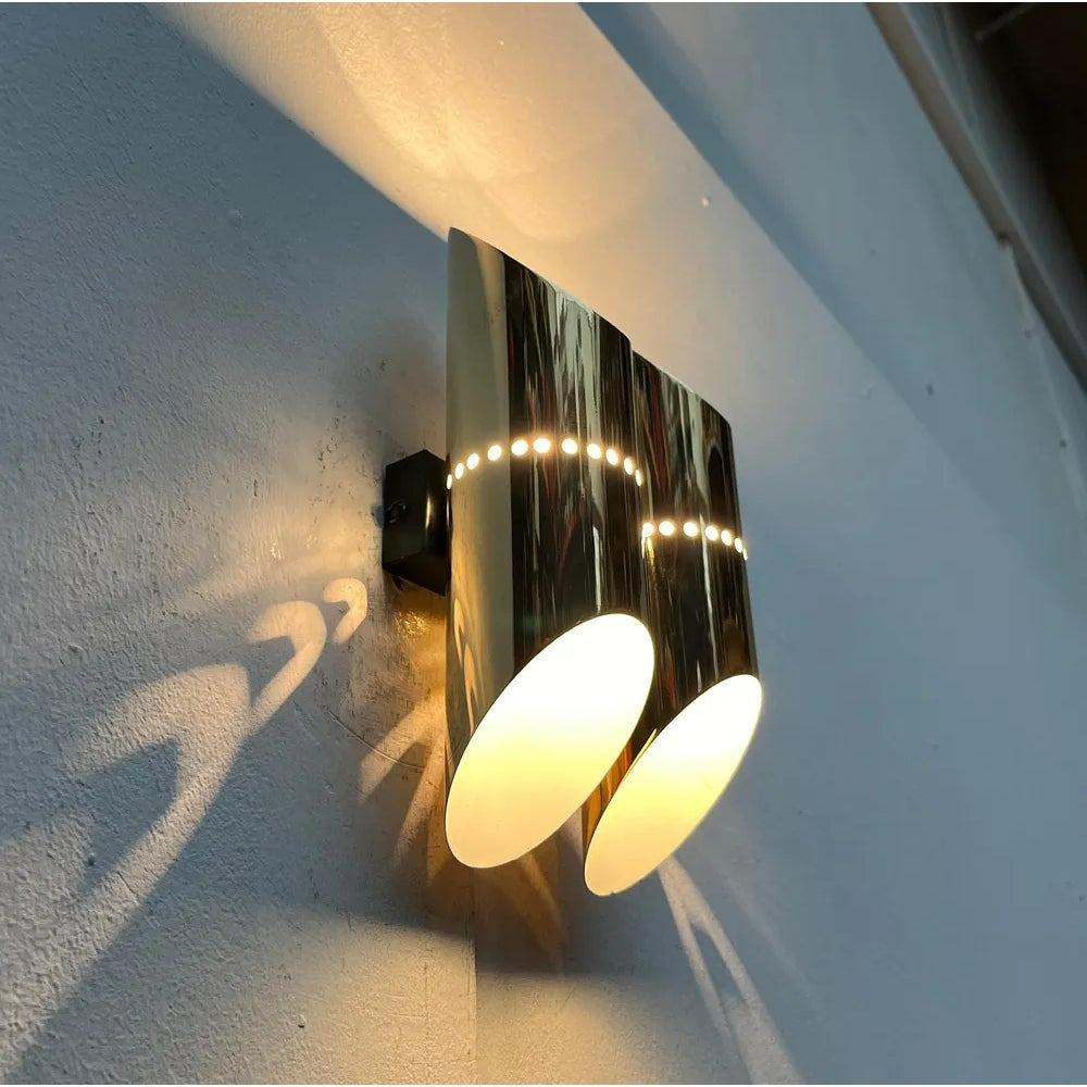 Rare Space Age wall lamp.

Two tubes cut on both sides are arranged parallel on a black base. There is a burning point in each pipe. The light comes out upwards and downwards. The only ornament is a central perforation on each tube, through which a