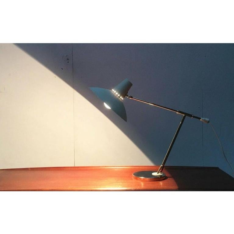 Rarissima lampada da tavolo della metà del secolo scorso. Probabilmente di Kaiser degli anni '50/'60.

La lampada convince per il suo design elegante e la sua matericità. Un braccio largo che viene tenuto in modo flessibile in un tubo. L'ombrello è