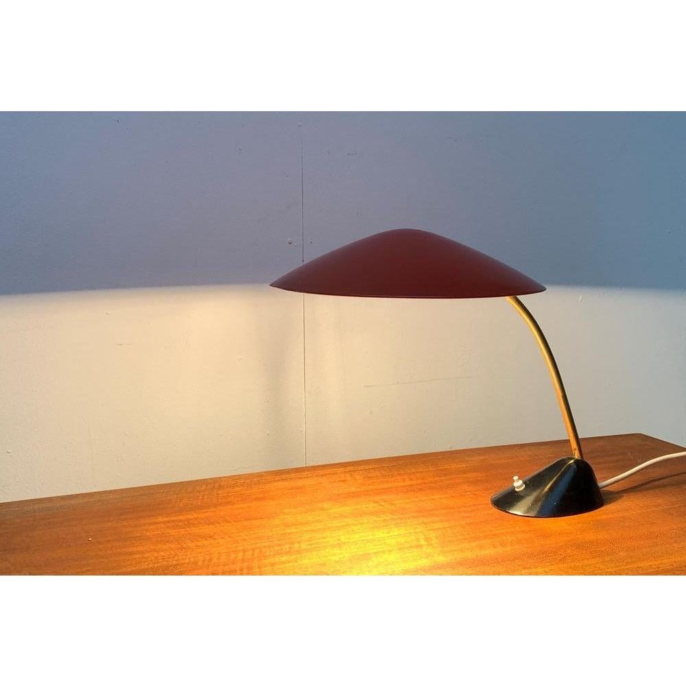 Mid-Century table lamp from Cosack.

An elegant design from the 50s. The flat shade has a striking dome. It is finished in red and tilts via a hinge. The heavy base features an asymmetrical cone shape and is painted black. The shade and base are