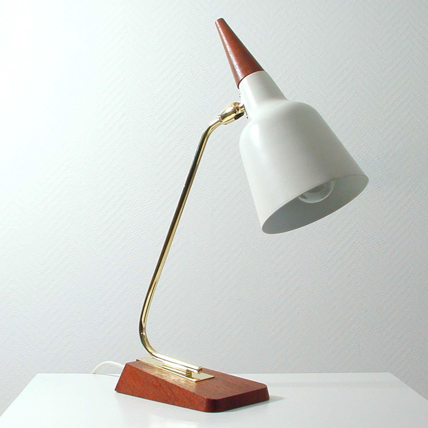 This very rare and elegant table or desk lamp was designed and manufactured in Germany in the 1950s by Kaiser Leuchten. It has got a teak and brass base, a brass lamp arm and a light cream / white lacquered metal adjustable lamp shade with teak