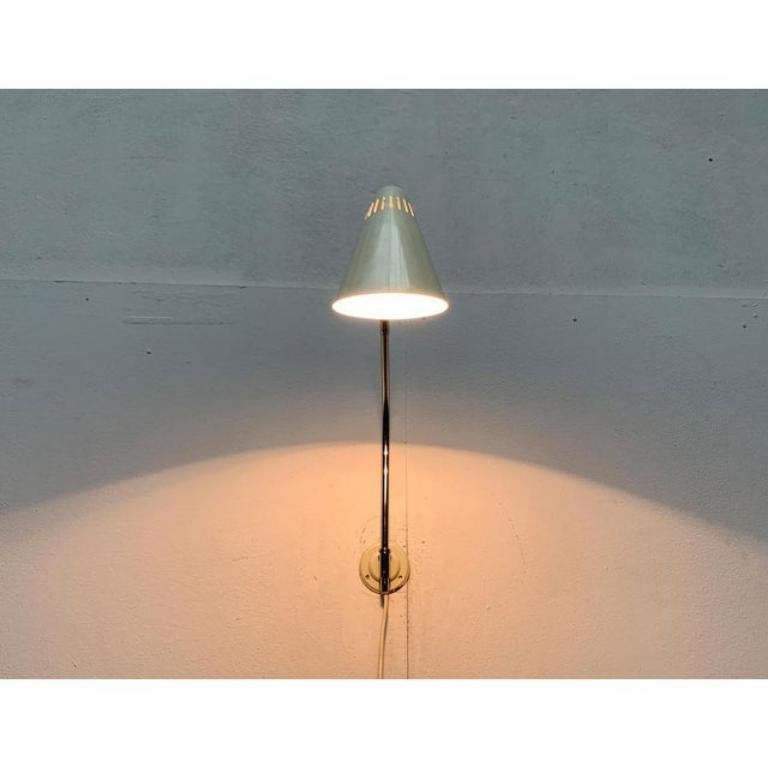 Lampada da parete del Mid Century di Kaiser Lets con un collo di cigno flessibile.

L'ombrello della lampada ha una semplice forma a cono. La cattedrale dell'ombrello è dotata di varie perforazioni che servono a controllare il calore. L'estremità