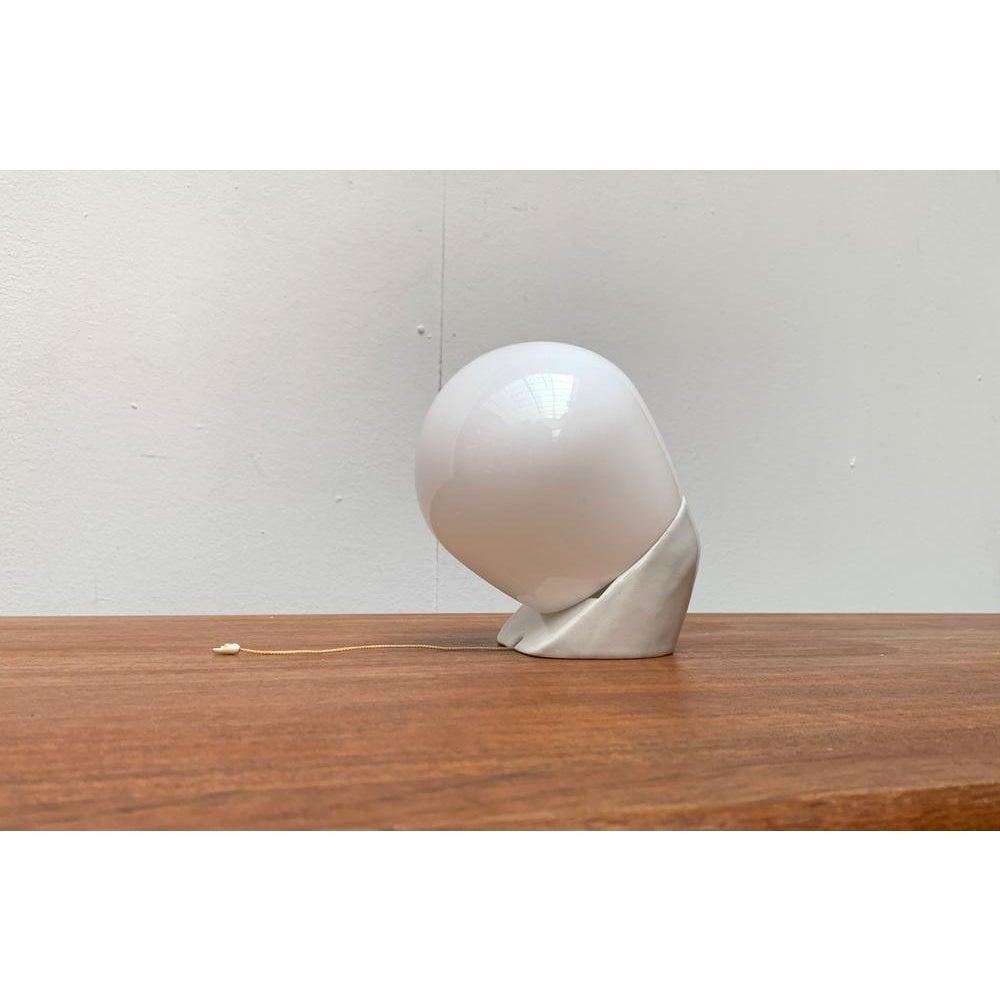 Classic wall lamp by Lindner after a design by Wilhelm Wagenfeld from the 50s.

A functional, elegant and thus timeless design. The pedestal is running in white. The screw is opal overturn. This piece has an attribution mark.
Up to 250V (Europe/UK