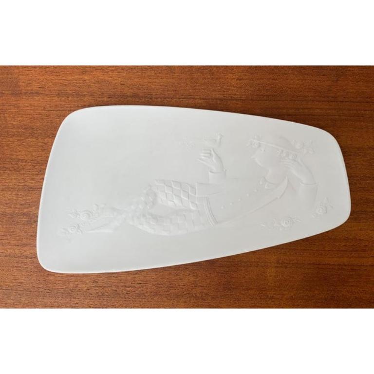 Elegante cuenco plano de porcelana blanca según un diseño de Bjørn Wiinblad de los años 60. Llama la atención la forma asimétrica con el borde ligeramente elevado. La superficie presenta un fino relieve con acabado mate. Esta pieza tiene una marca