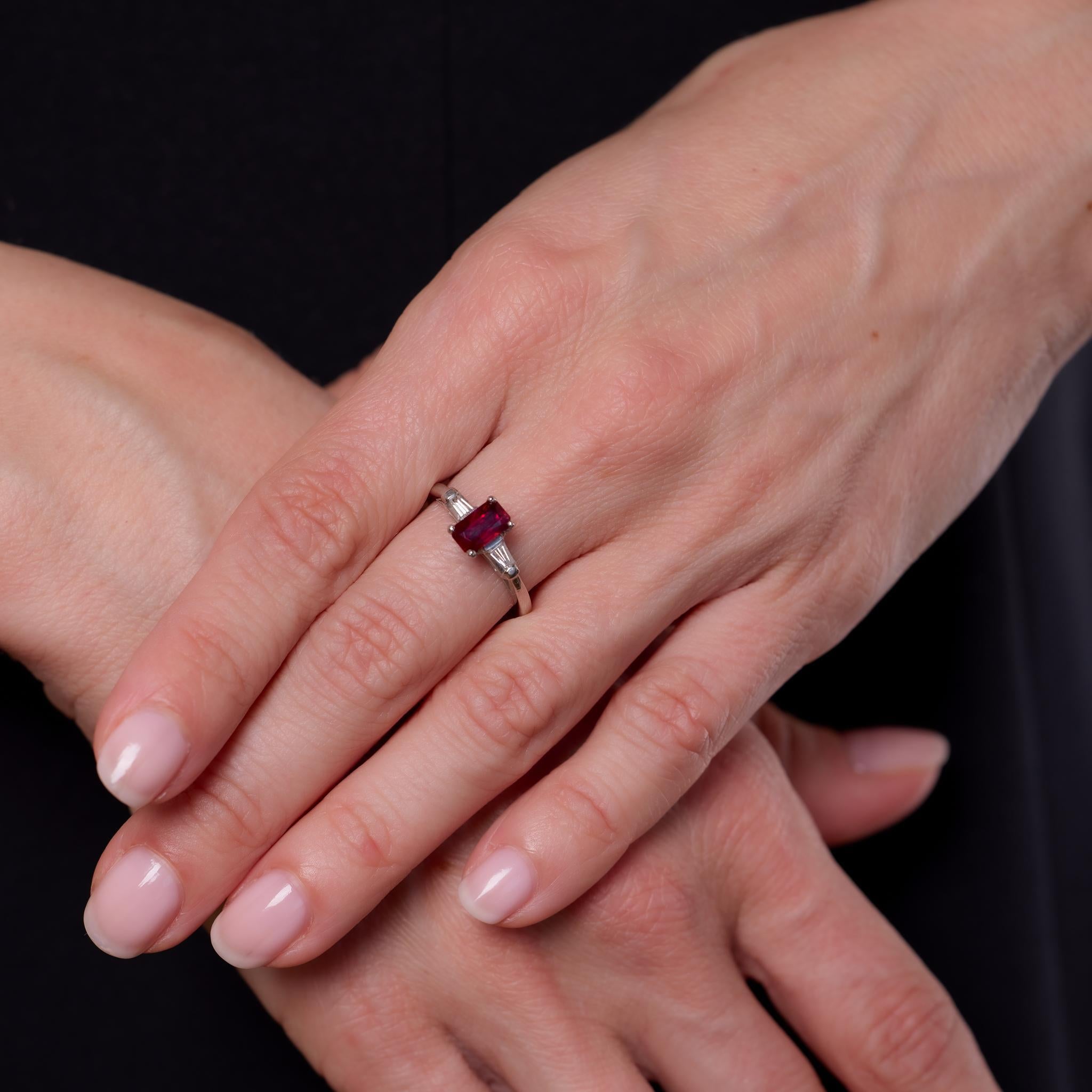 Crafted in the 1950s, this Mid Century platinum ring centers a GIA-certified 1.25-carat octagonal cut ruby from Thailand, enhanced with heat treatment to enrich its vibrant red hue. The ruby is flanked by two baguette cut diamonds totaling