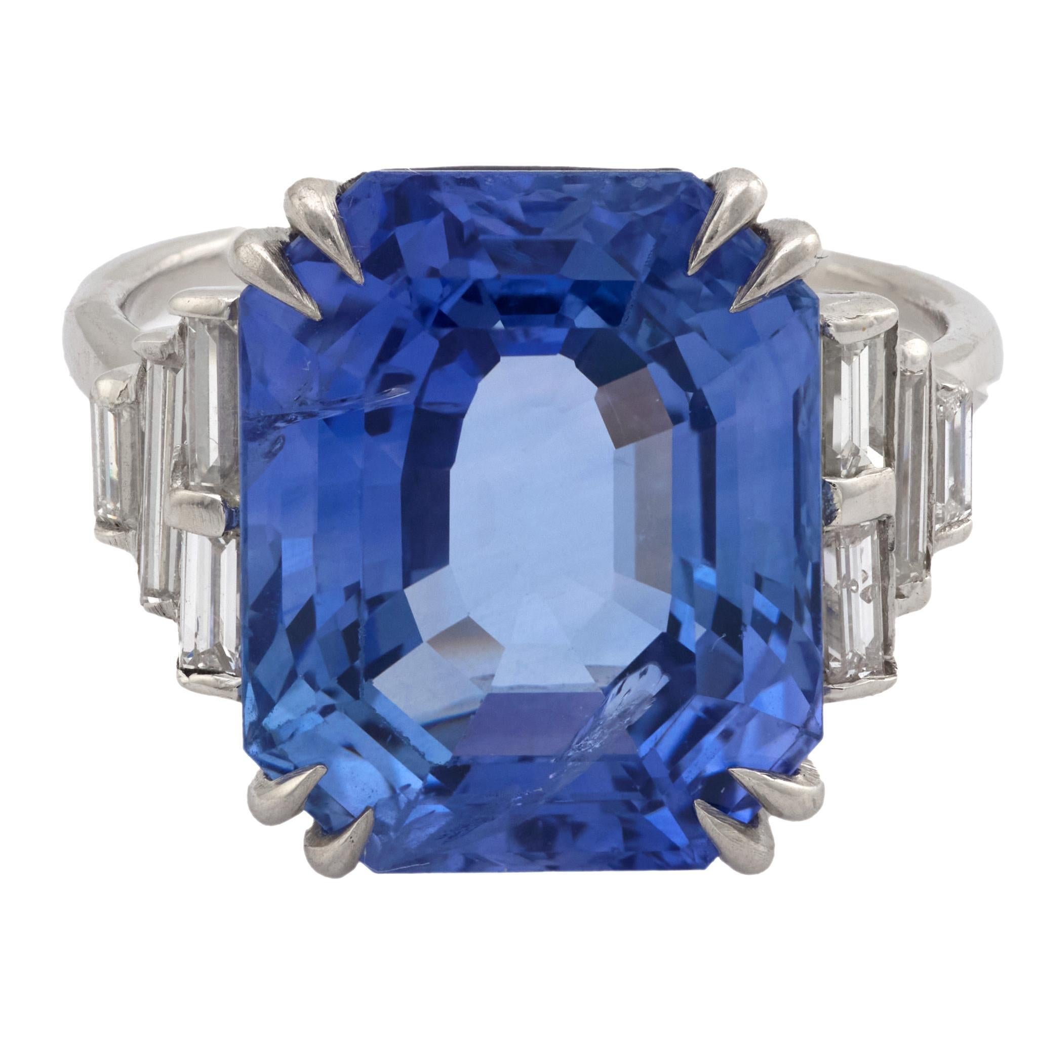 Este anillo de platino de mediados de siglo de la década de 1950 exhibe un llamativo zafiro de talla octogonal de 12,64 quilates de origen ceilanés, certificado por el GIA #2231608852 como calentado. Ocho diamantes talla baguette, con un total