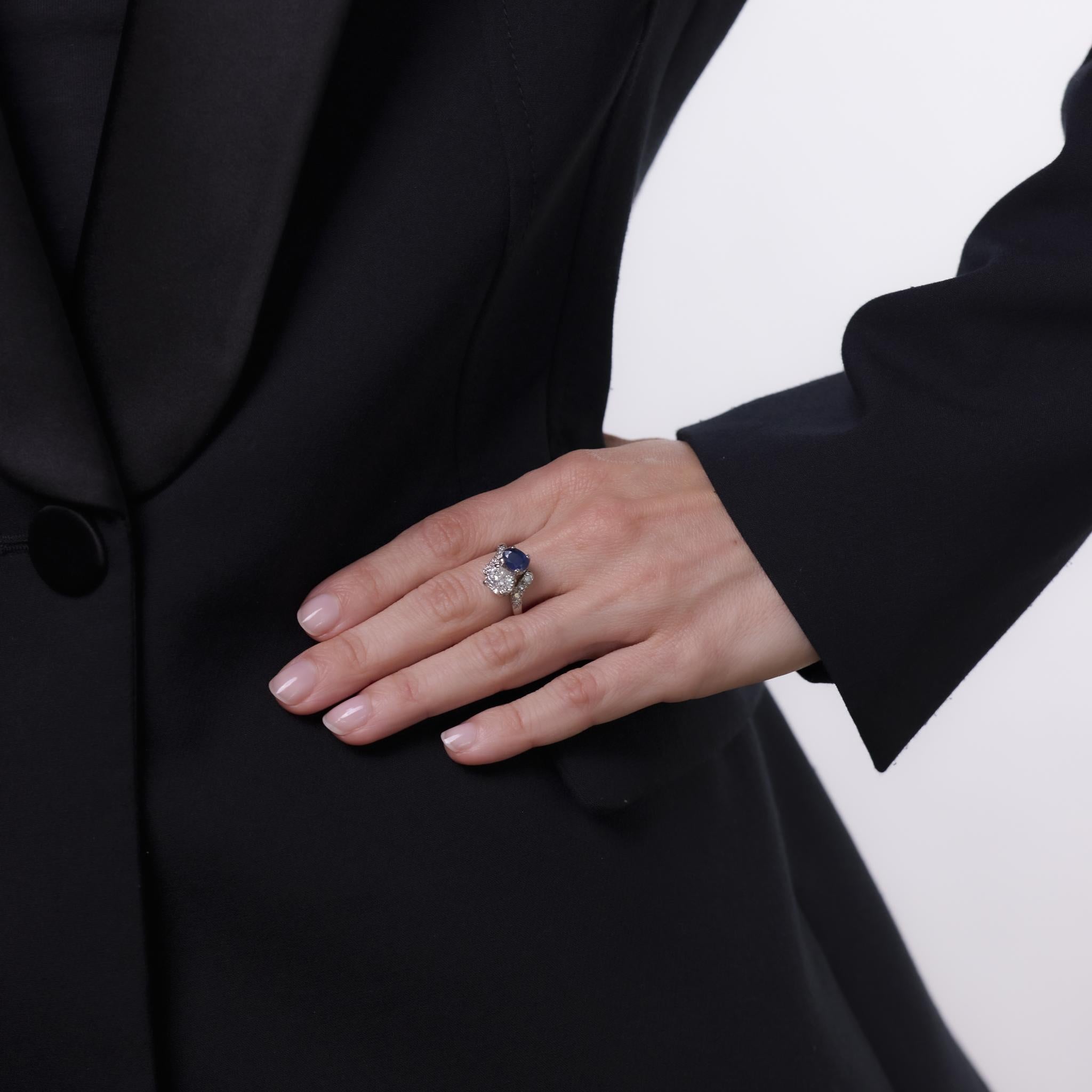 Questo anello in platino del Mid Century degli anni '50 mette in mostra un diamante taglio old mine da 1,41 carati, certificato da GIA (#6237547762) con colore J e purezza I2. Accanto ad esso è incastonato uno zaffiro blu dal taglio ovale di circa 1