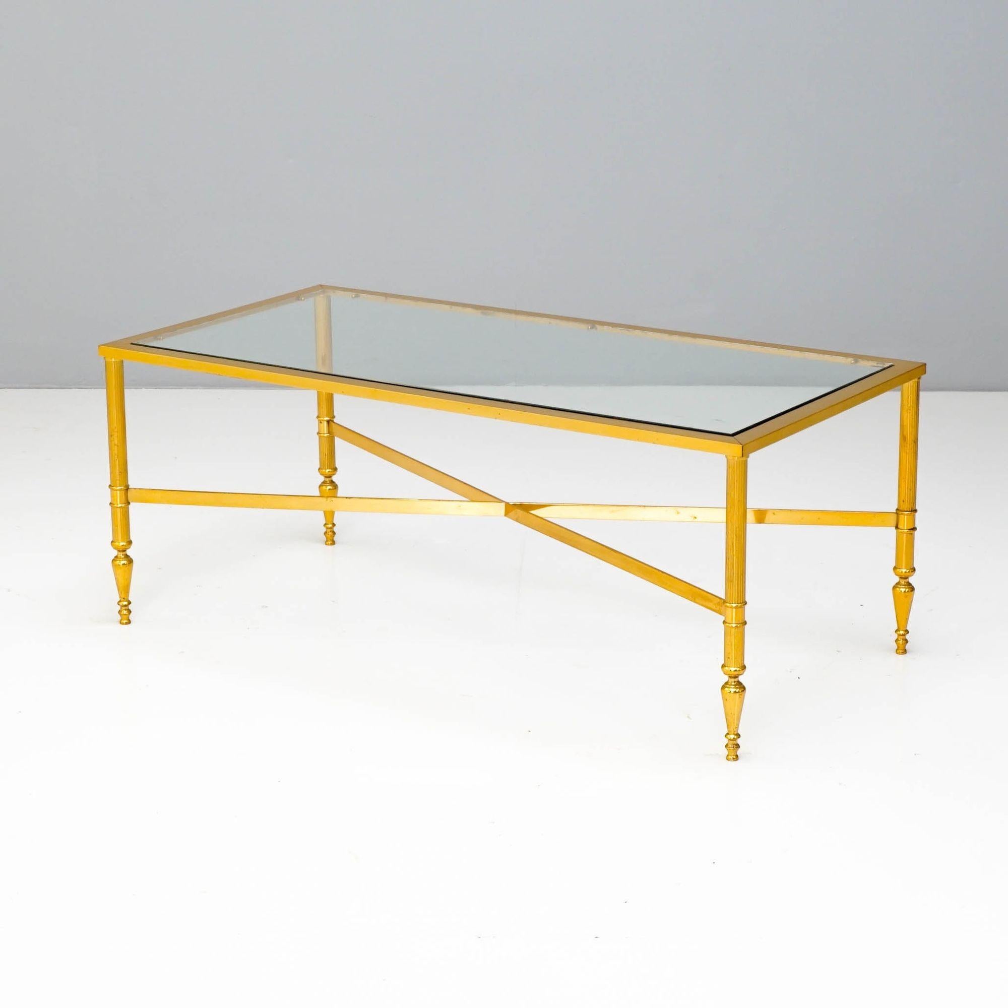 Table basse à plateau en verre sur une base en laiton doré avec un piétement en forme de x.