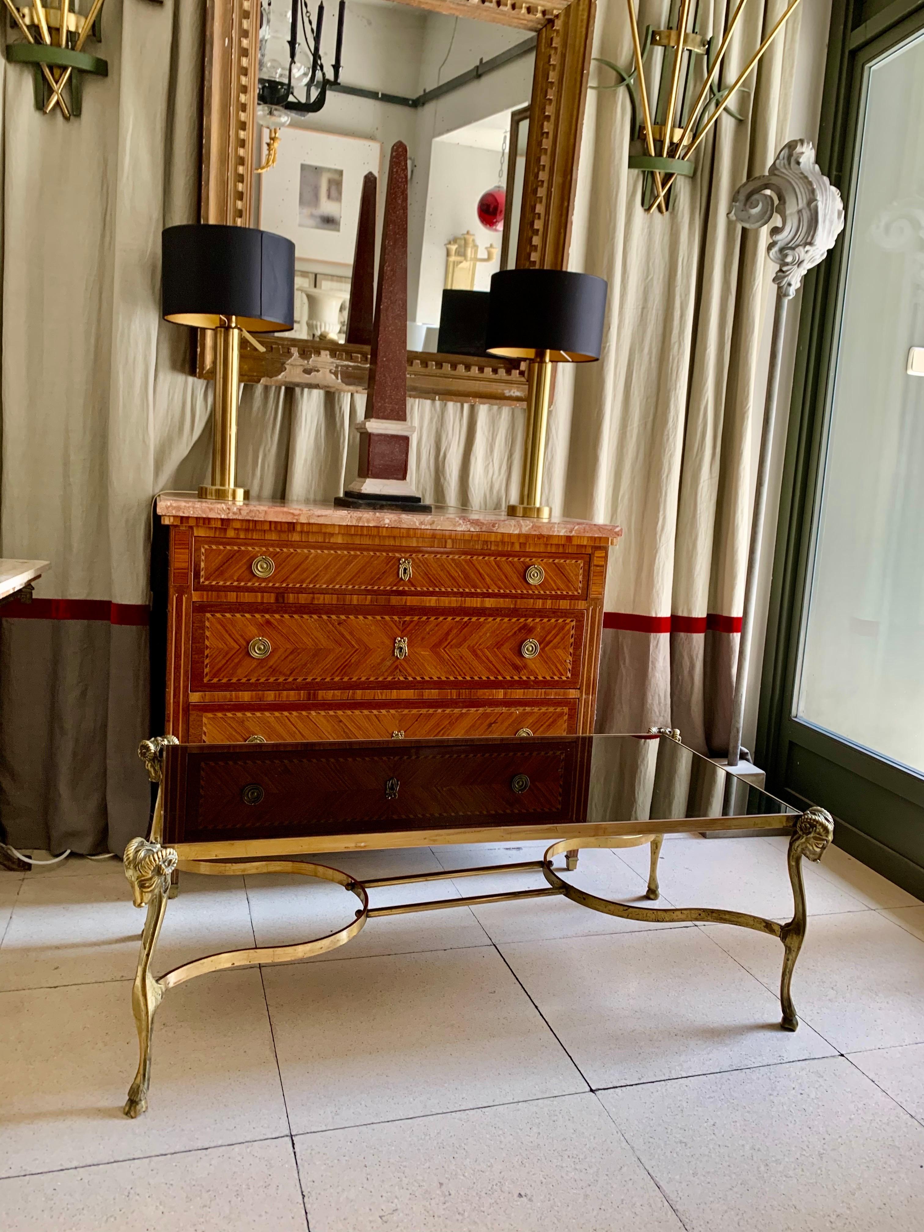 Table basse en bronze doré, style Jansen, avec plateau en verre noir. Le verre noir est encadré de nervures en bronze doré et est soutenu par quatre pieds à tête de bélier, de style néoclassique.