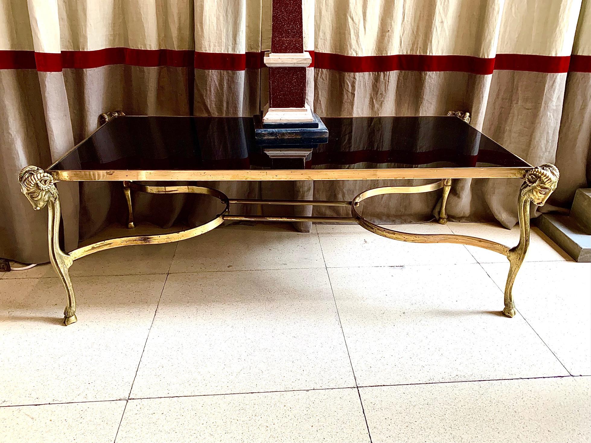 French golden bronze coffee table with balck glass top. The black glass is framed with gilden bronze ribs and is supported by four legs with ram heads, in neoclassical style.
