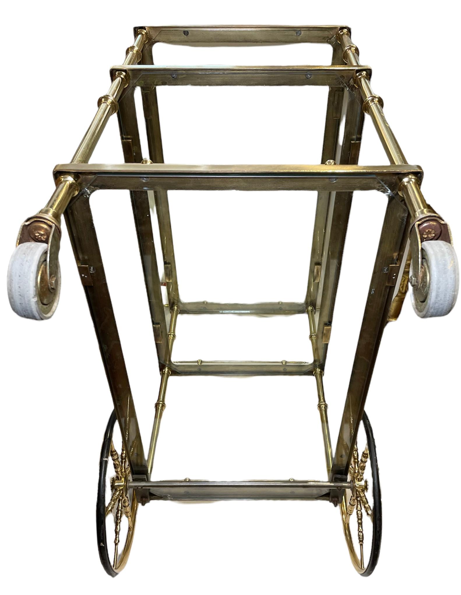 This is a three tiers bar cart. It depicts a gilt bronze cart with three original rectangular glass tiers supported in each corner by four cylindrical tubes. Each one of the tier has a gilt gallery made of thin cylindrical tubes, too. The cart has a