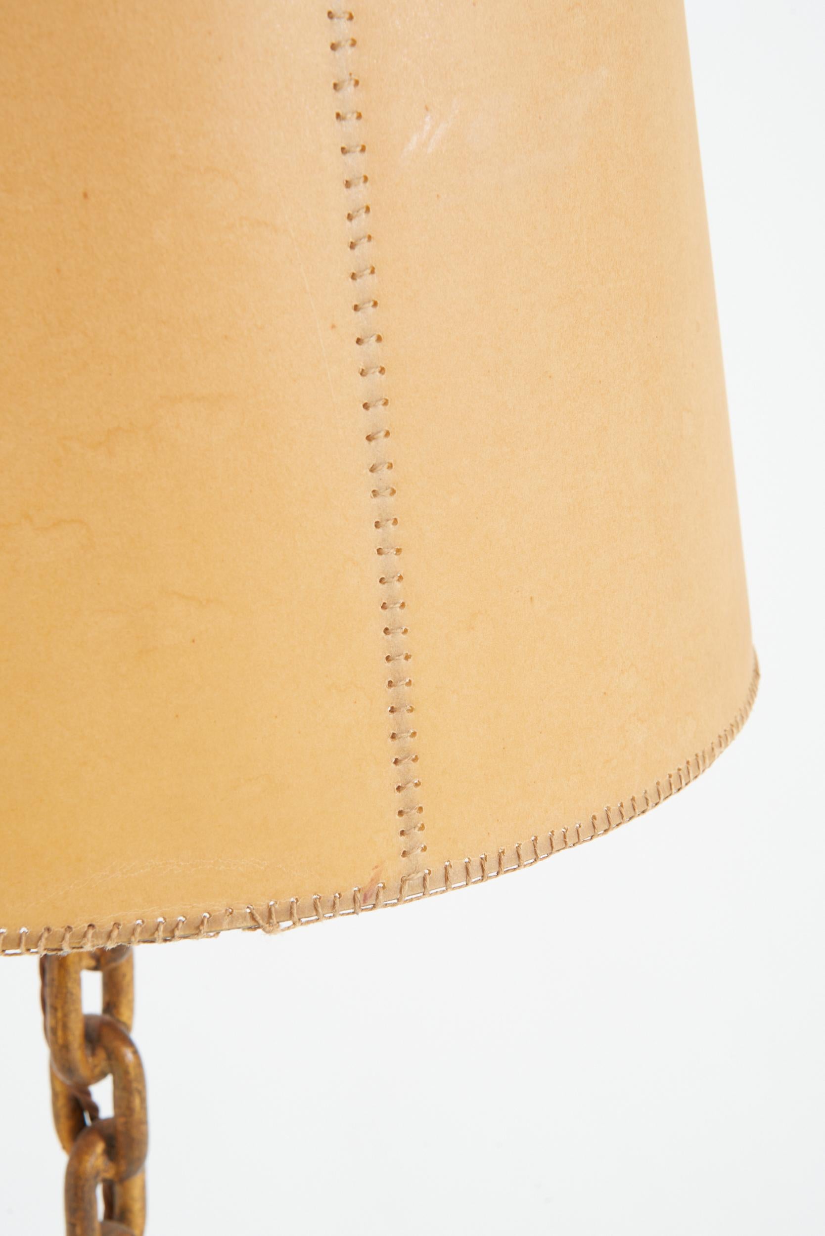 A gilt iron chain-link floor lamp, with its original parchment shade
Spain, mid 20th Century
With the shade: 155 cm high by 44 cm diameter 
Lamp base only: 138 cm high by 34 cm diameter