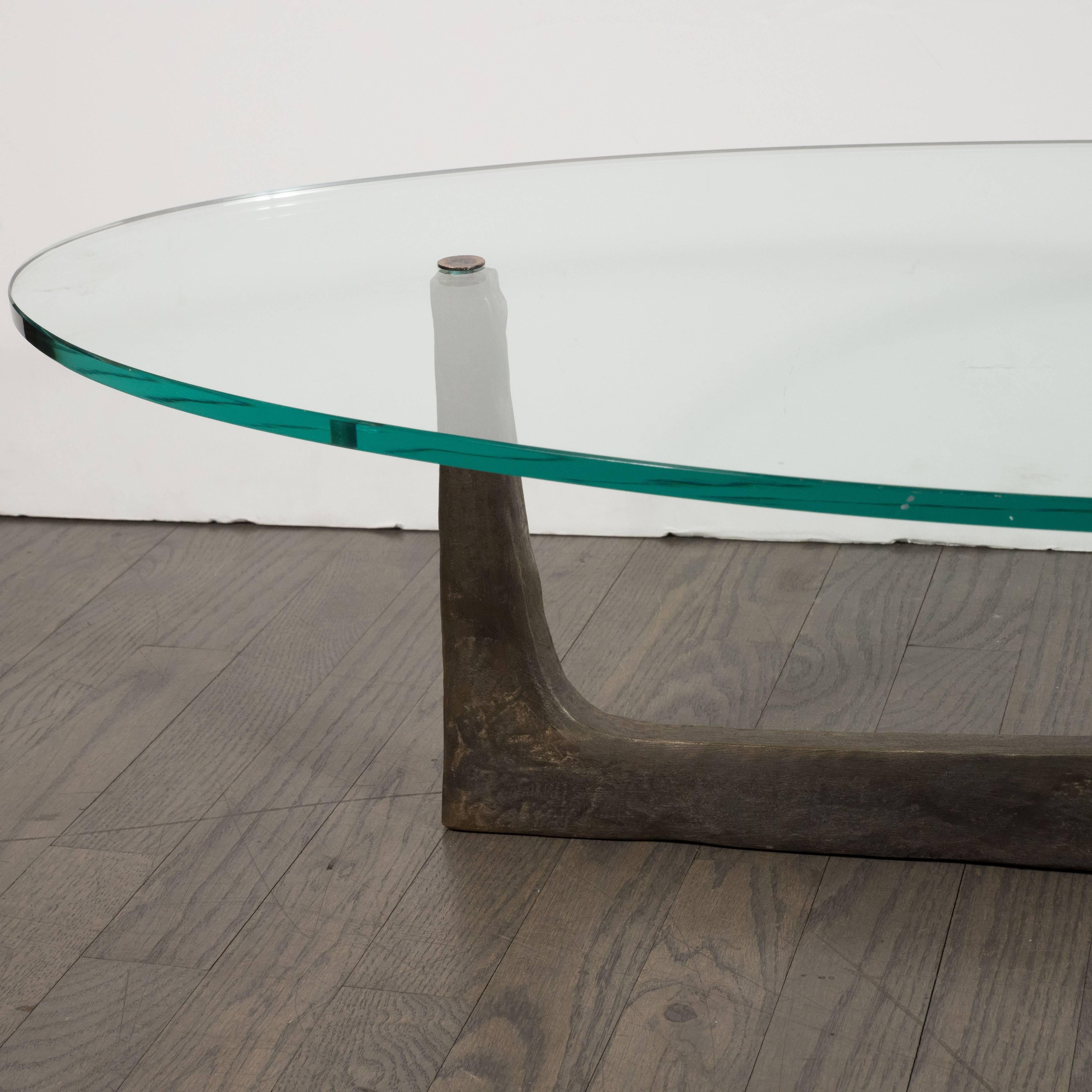 This graphic and sophisticated cocktail table was realized by the renowned artisan Felix Agostini, circa 1960. Suggesting the work of Isamu Noguchi, the piece features three tapered curvilinear arms in patinated bronze that support an oval plate