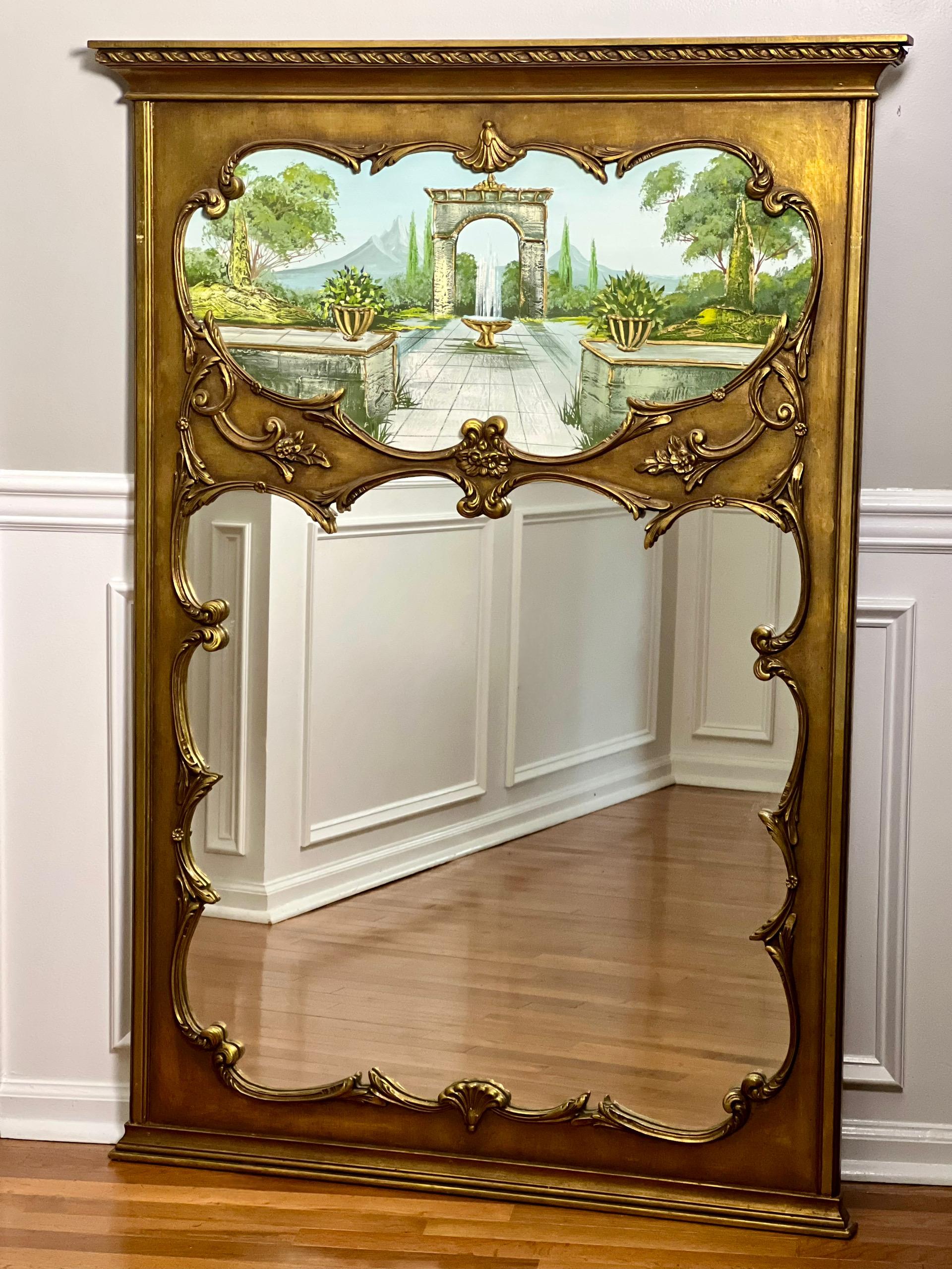 Specchio Trumeau in legno dorato della metà del secolo scorso con dipinto un tranquillo giardino. Presenta una cornice in legno dorato intagliato con motivi floreali a scorrimento e uno stemma a conchiglia. La scena pacifica dai colori vivaci