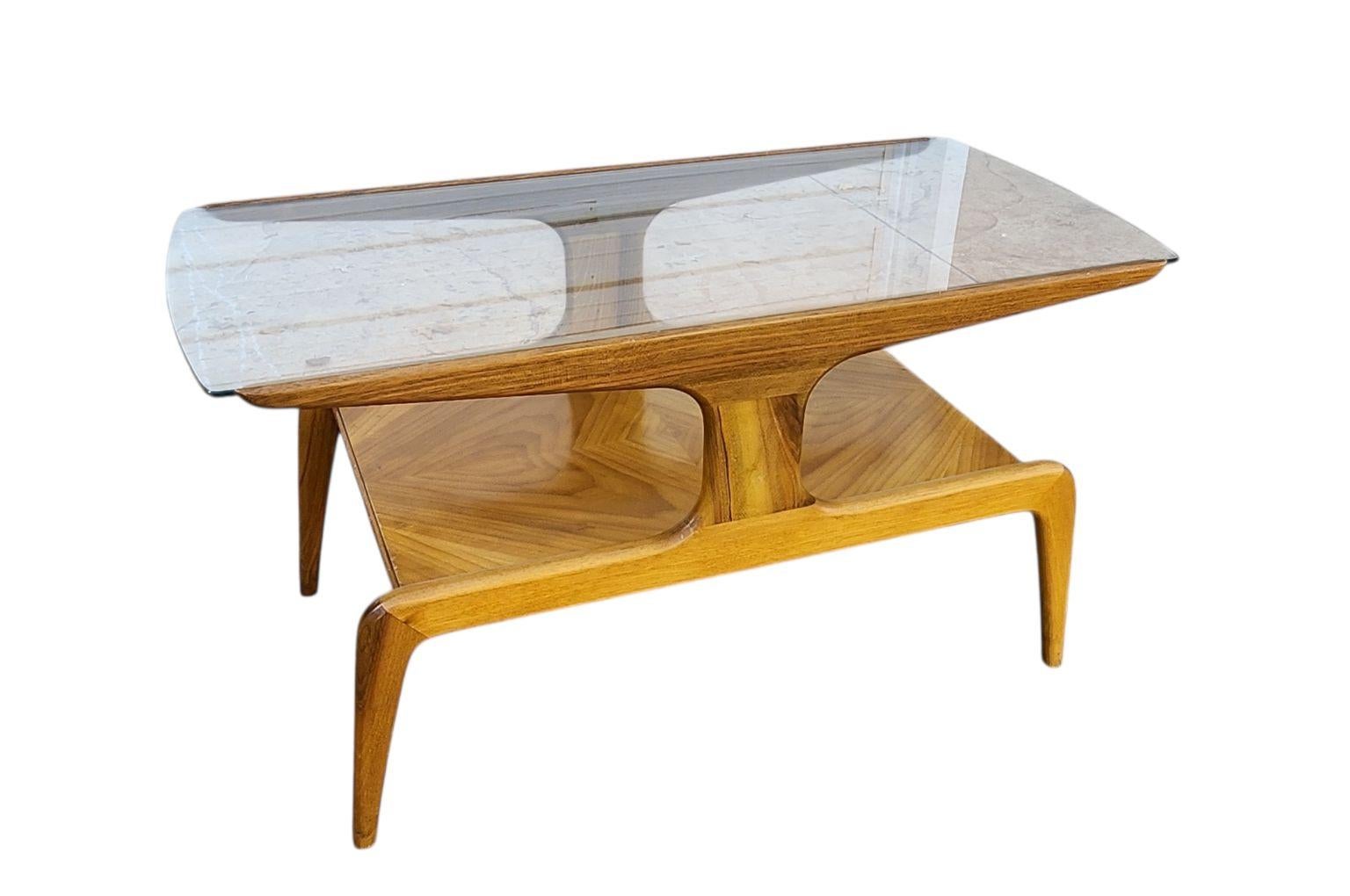 Icónica mesa de centro de uno de los arquitectos italianos más importantes de todos los tiempos, Gio Ponti. Una mesa maciza de nogal caramelo fabricada por Domus Nova. Tiene esa forma elegante de Gio Ponti con una elegante superficie de cristal en