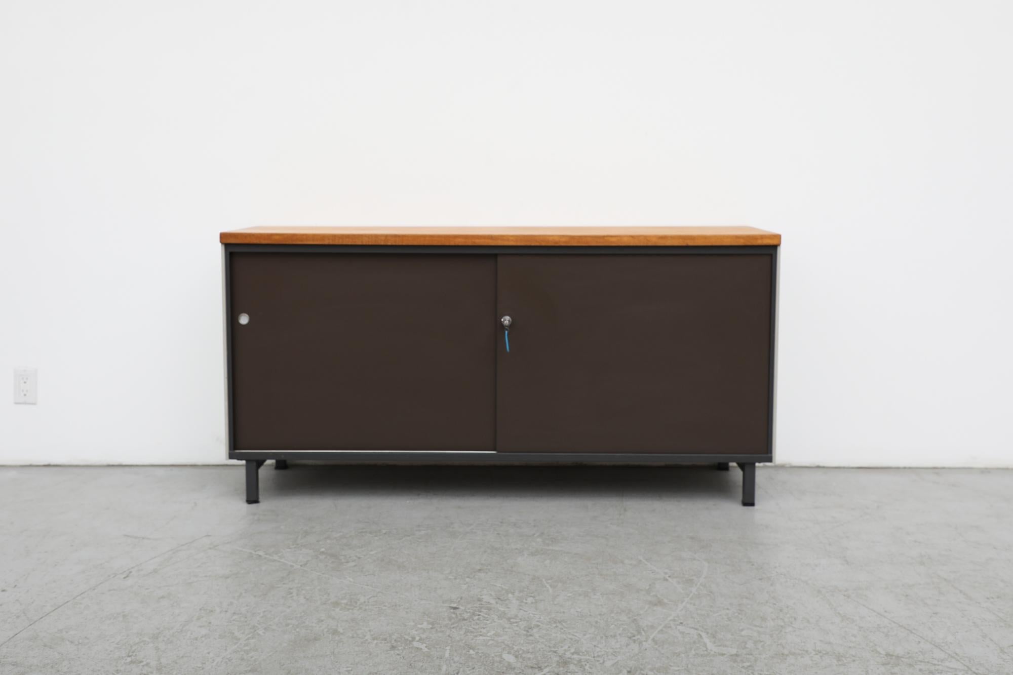 Famed Mid-Century Dutch furniture manufacturer Gispen made industrial cabinet with light grey enameled metal frame, brown metal sliding doors and wood top. The doors have handsome, inset round metal pulls and  are outfitted with lock and key. In