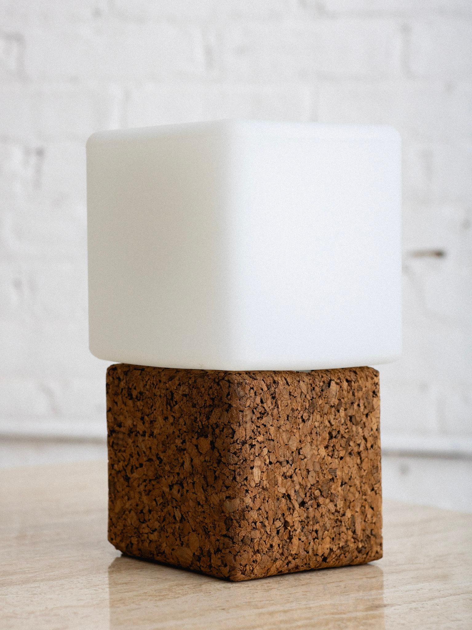 A mid century table lamp constructed of cork with a glass shade. Cube form silhouette. Upper glass simply rests over the lightbulb onto cork base.