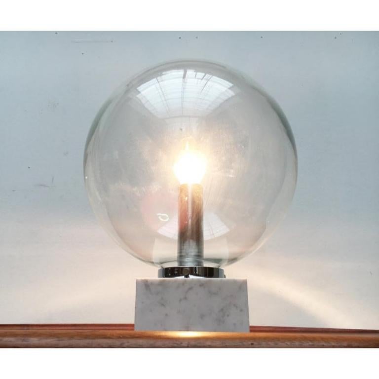 Impressive glass ball table lamp from the renowned house Erco.

The bright marble base, on which a large ball of clear glass sits, catches the eye. The glass has a diameter of 40cm, the heavy base is 16x16cm. The glass ball is attached to the base