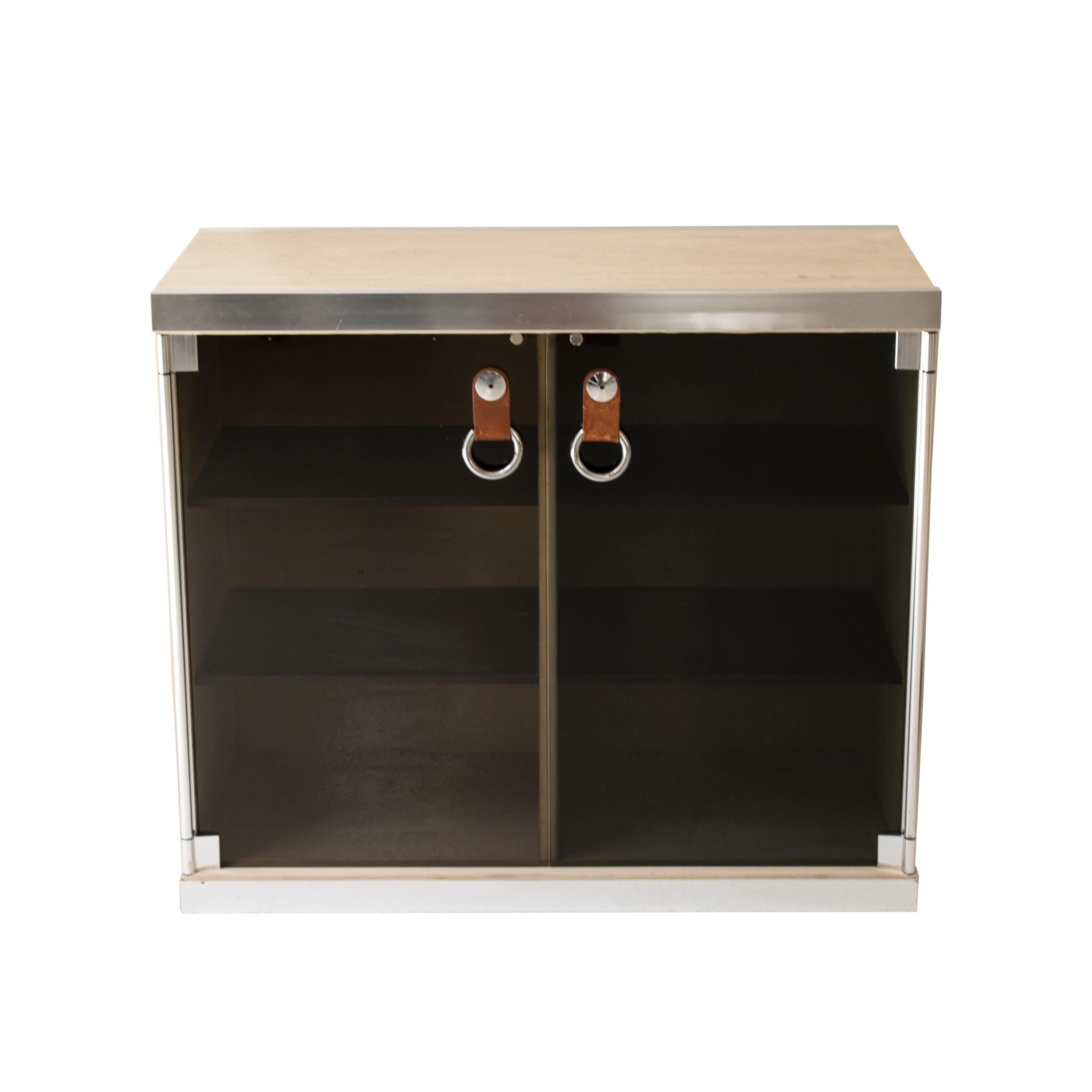 Mid-Century Modern cabinet designed in 1970 by the Italian designer Guido Faleschini for Hermes. 

The cabinet consists of a metal frame, a travertine marble top, and a beige velvet cover on the sides.

The double door is made of black tinted glass,