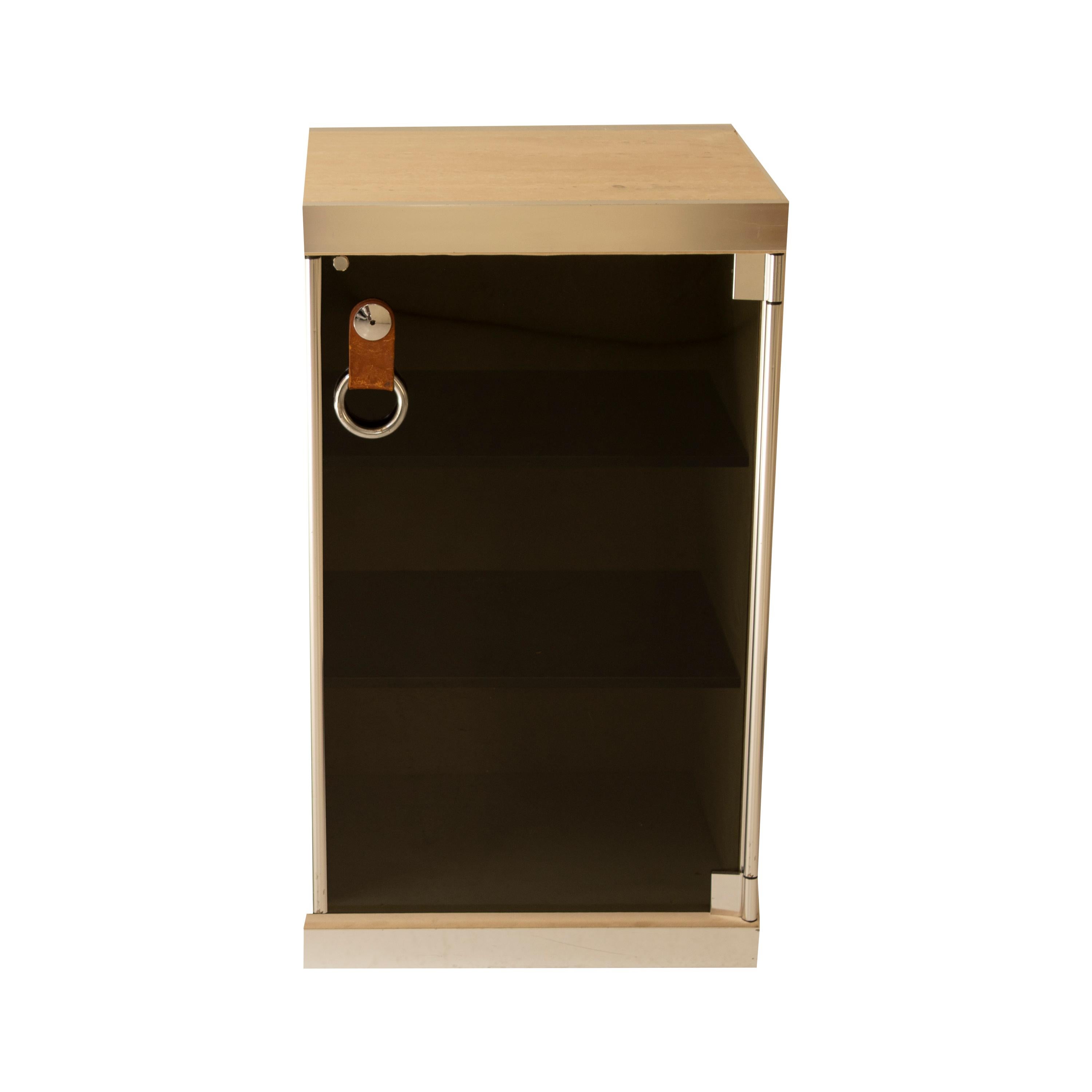 Mid-Century Modern cabinet designed in 1970 by the Italian designer Guido Faleschini for Hermes. 
The cabinet consists of a metal frame, a travertine marble top, and a beige velvet cover on the sides.
The door is made of black tinted glass, with