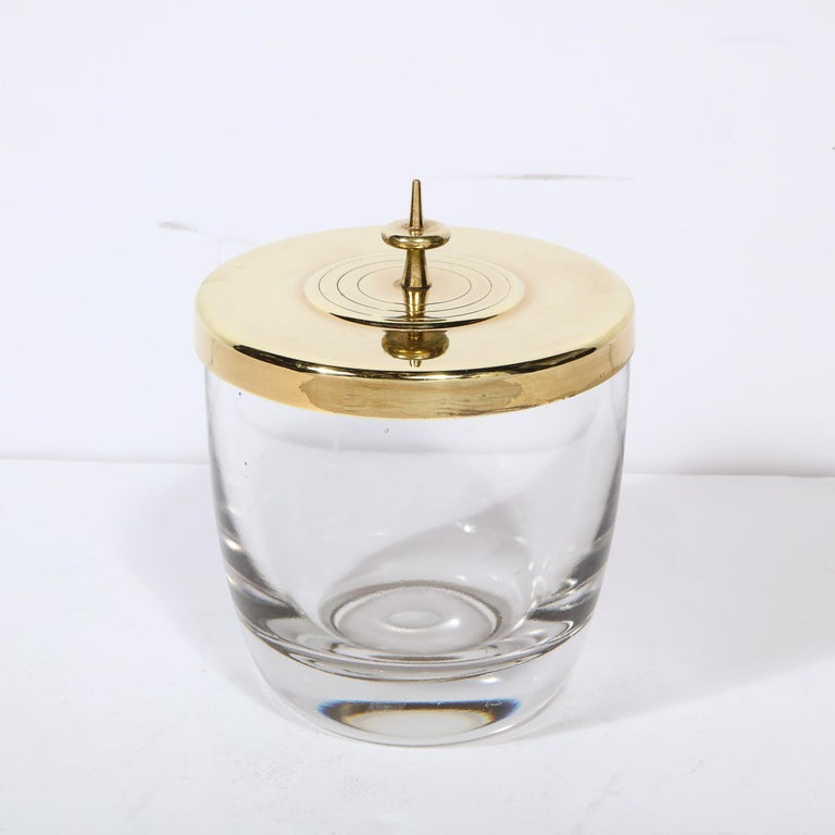This gorgeous Mid-Century Modern ice bucket was designed by Tommi Parzinger for Dorlyn Silversmiths circa 1950. It features a translucent glass body and a circular brass top with banded detailing at its center and an undulating sculptural finial