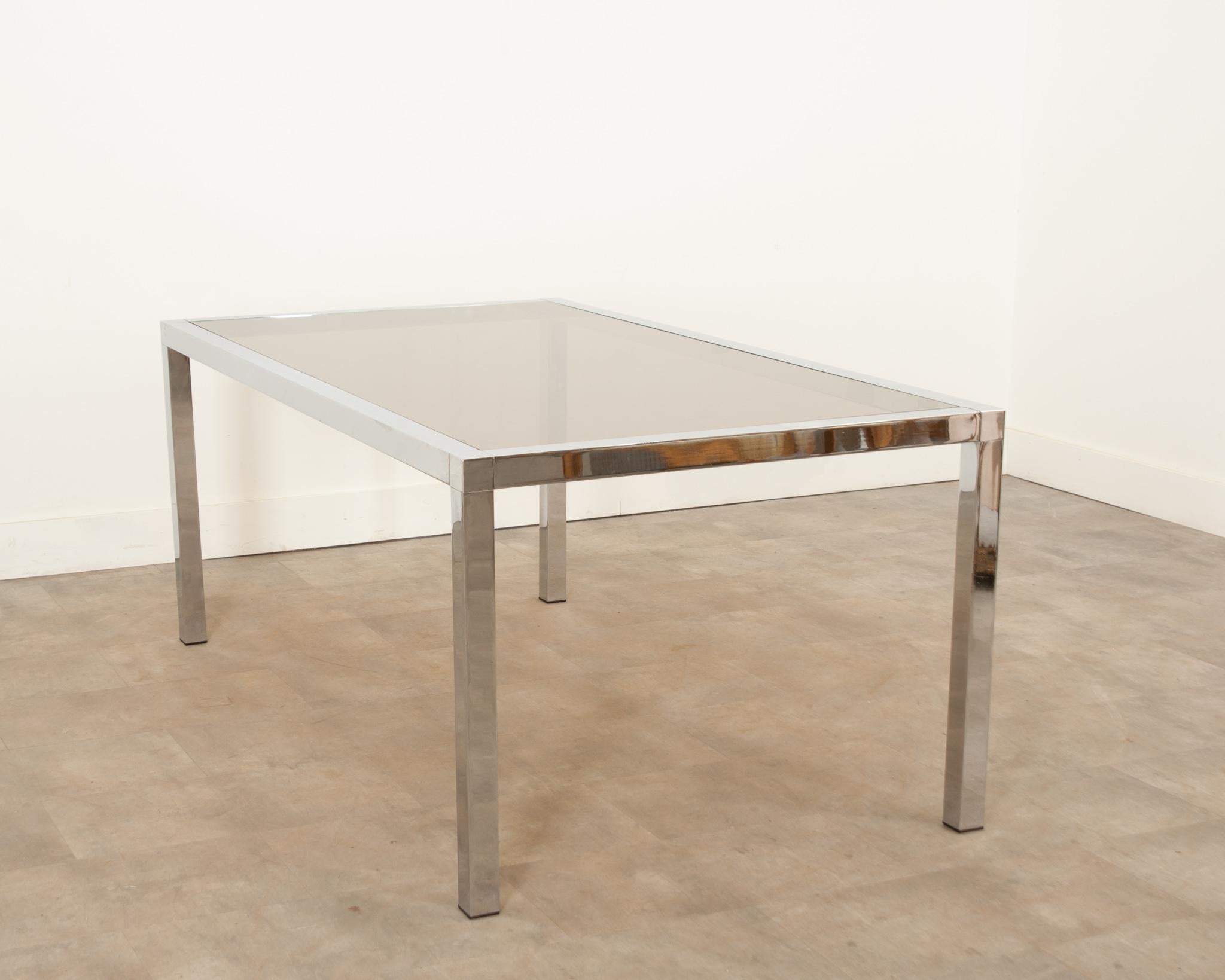 A French Mid-Century Modern dining room table in wonderful vintage condition. The large single pane of tinted glass is removable and fits seamlessly into the chrome frame. The rectangular frame has very minor wear and is capped with four protective
