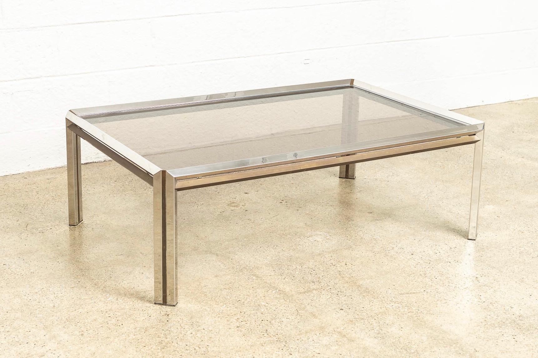 This Vintage Mid-Century Modern chrome, brass and glass rectangular coffee table in the style of Milo Baughman is circa 1970. The unique design features a faceted chrome frame accented by solid brass side bars and inlaid brass striped legs. The