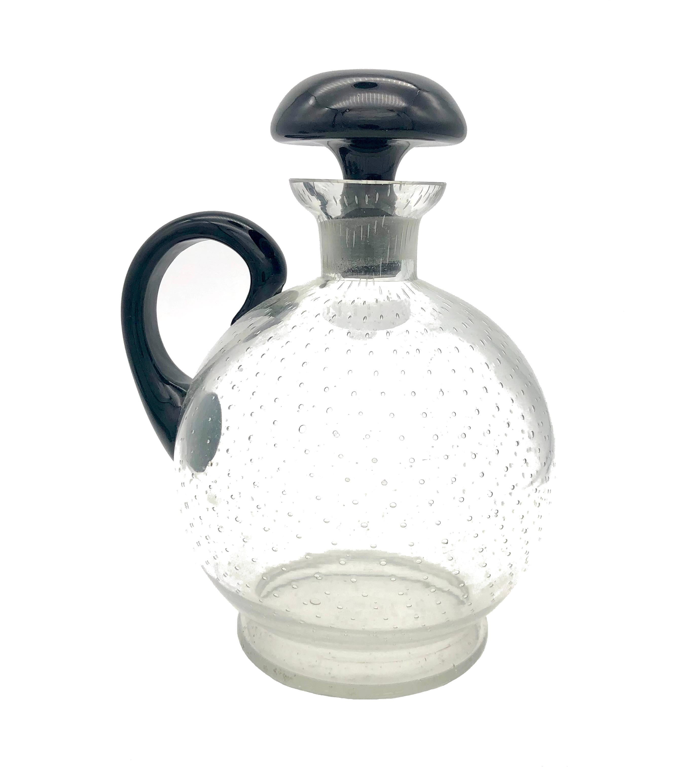 This stylish and well balanced little mid-century modern decanter has been handcrafted out of clear and black glass in the 1950/60's. The black stopper has been partially frosted.
The boddy of the decanter features on its entire surface an airbubble