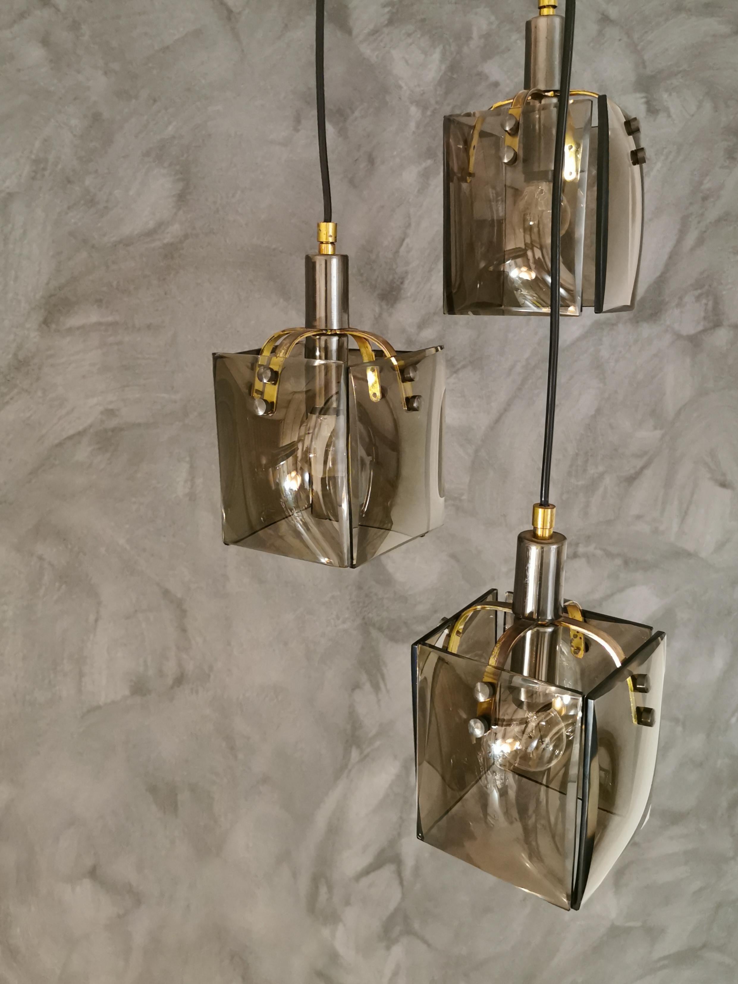 Chandelier made up of 3 pendants, each with four elegant smoked beveled glasses with brass and nickel-plated brass accessories, all supported by a ceiling disc. Good quality and good manufacturing. Italy in the 60s.