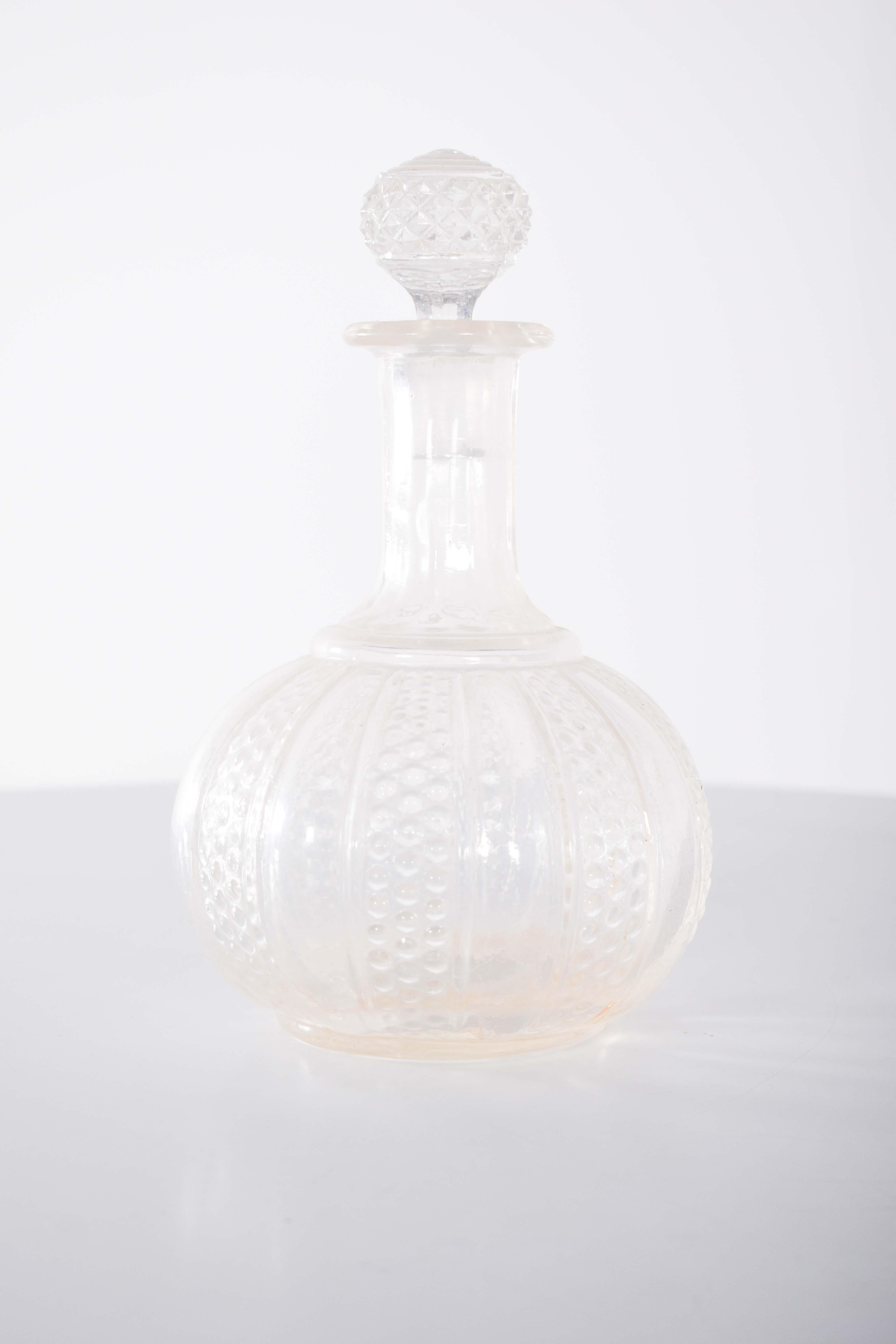 Bouteille de liqueur en verre. Ventre et CAP taillés en diamant. Avec un corps arrondi, il présente un beau travail en relief, avec des motifs verticaux alternant une texture lisse et une texture pointillée.
La transparence du verre permet