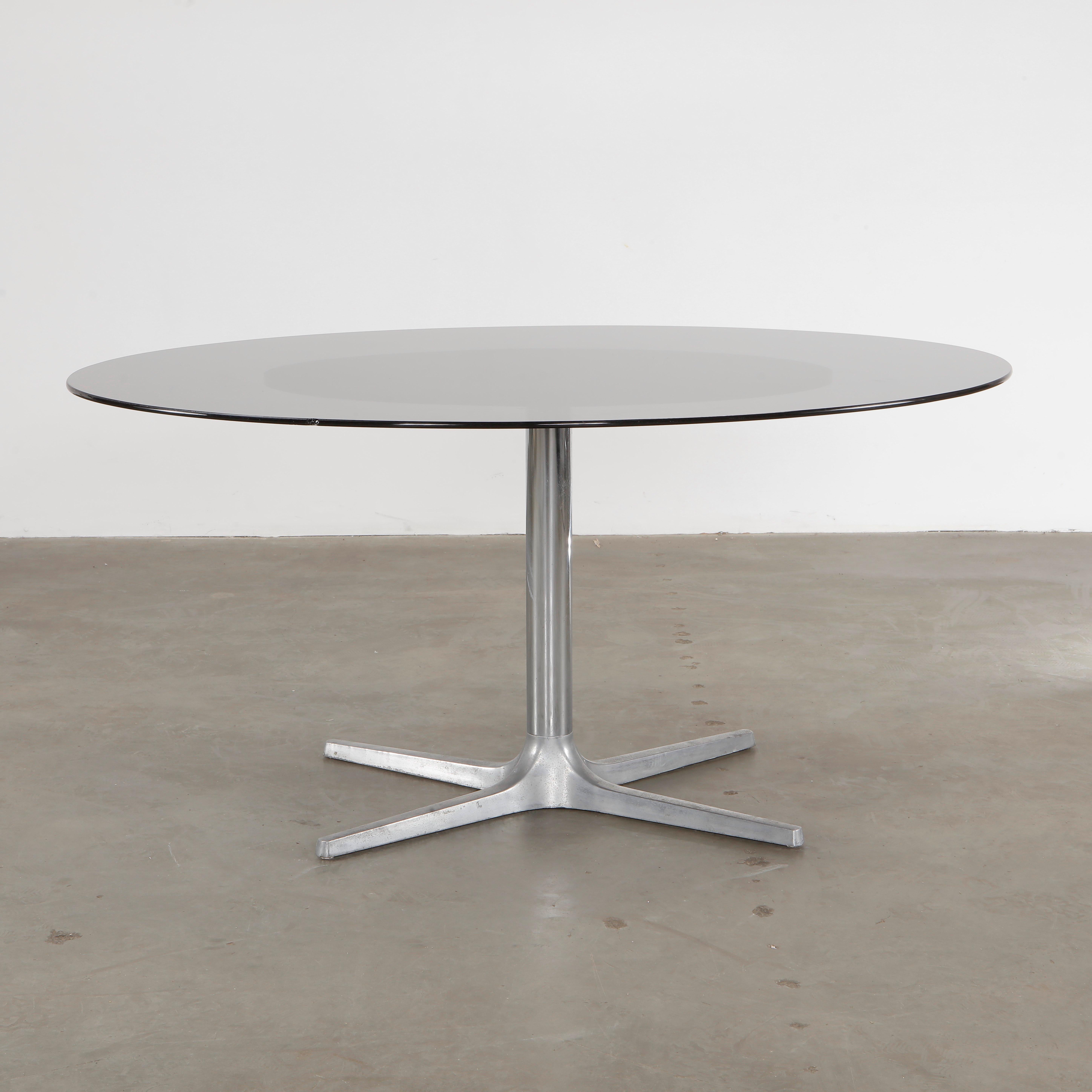 A sleek, modernist dining table with a tinted glass top and a metal cross-base. Height: 28 in. Width: 60 in. Depth: 46 in.